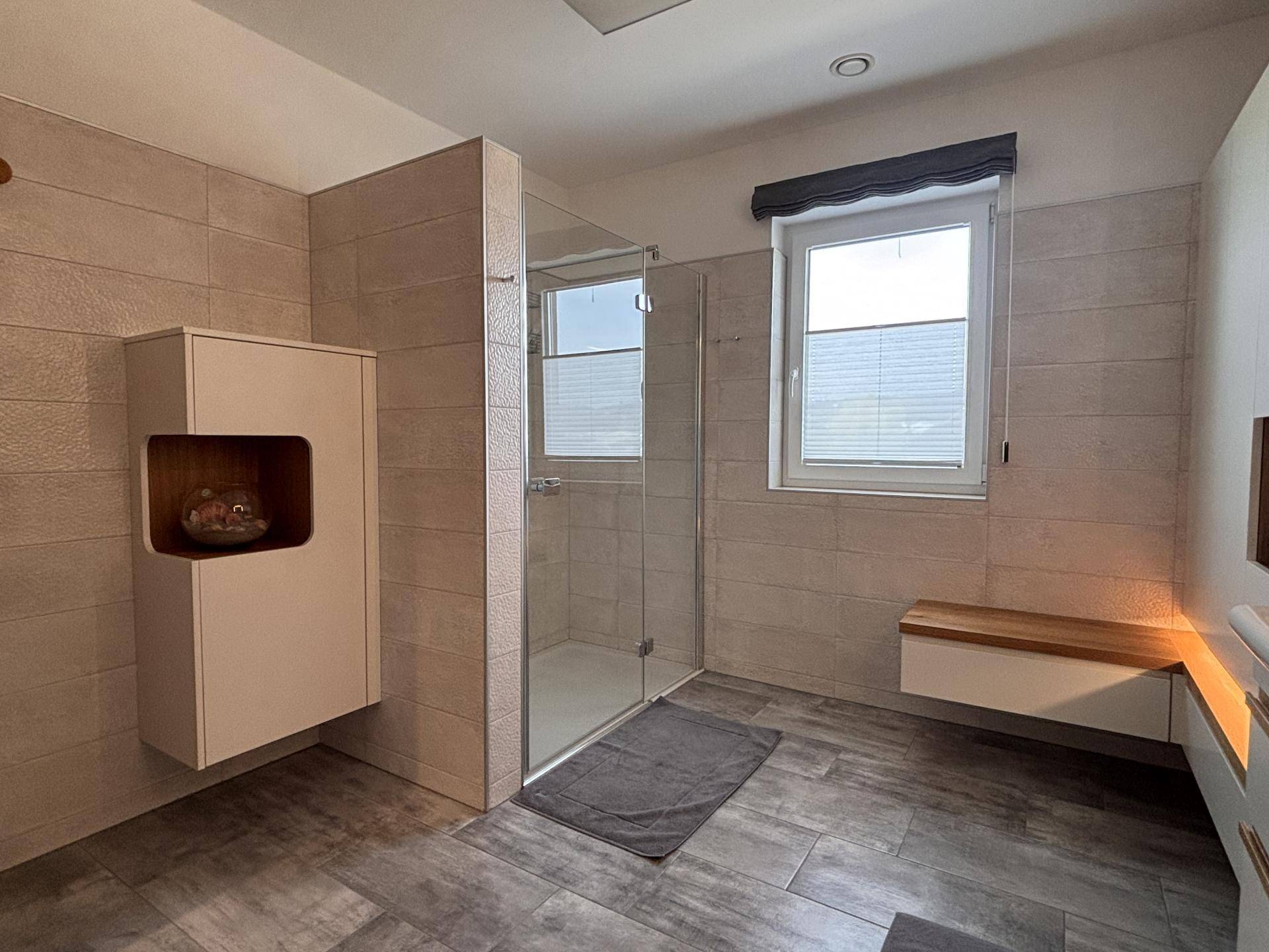 Geräumiges Badezimmer mit begehbarer Dusche, Glasabtrennung und Fenster.