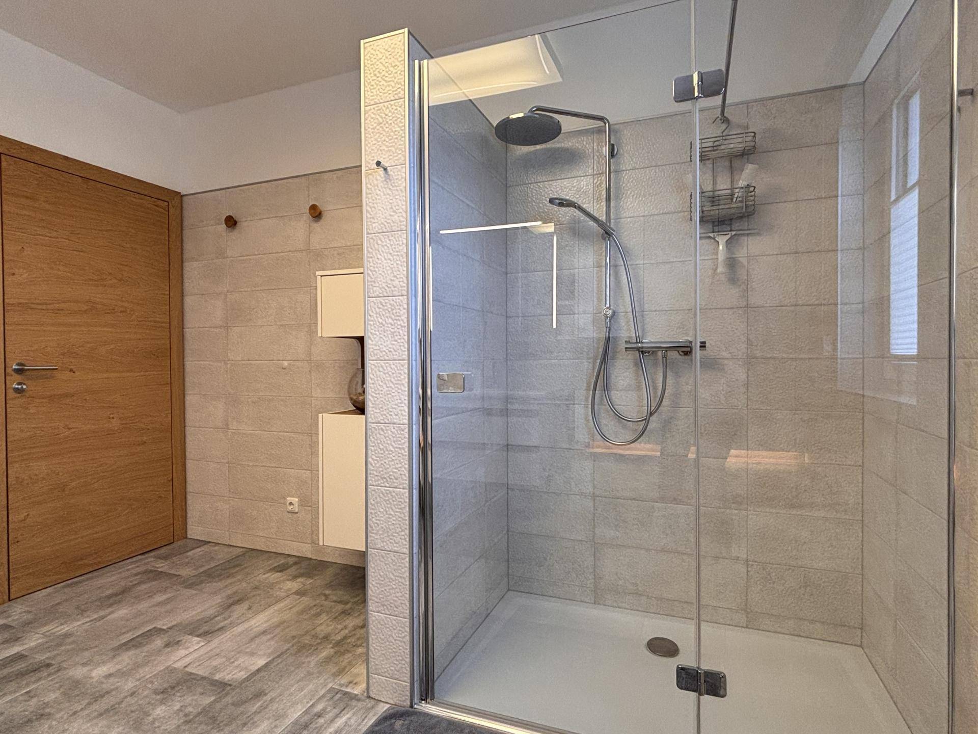 Begehbare Dusche mit Glasabtrennung, Regenduschkopf und modernen Fliesen.