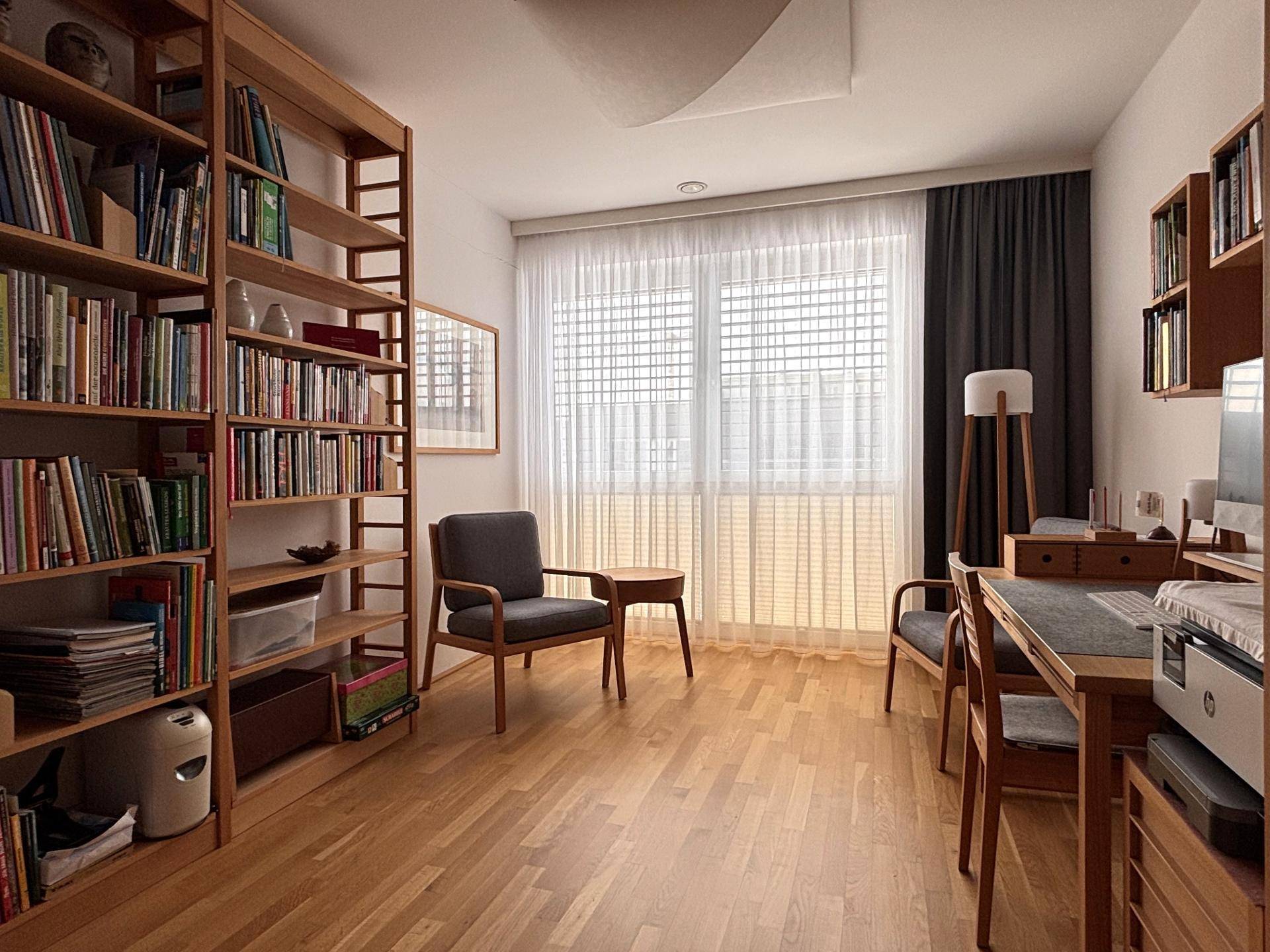 Helles Arbeitszimmer mit Bücherregalen, Holzfußboden und großem Fenster.