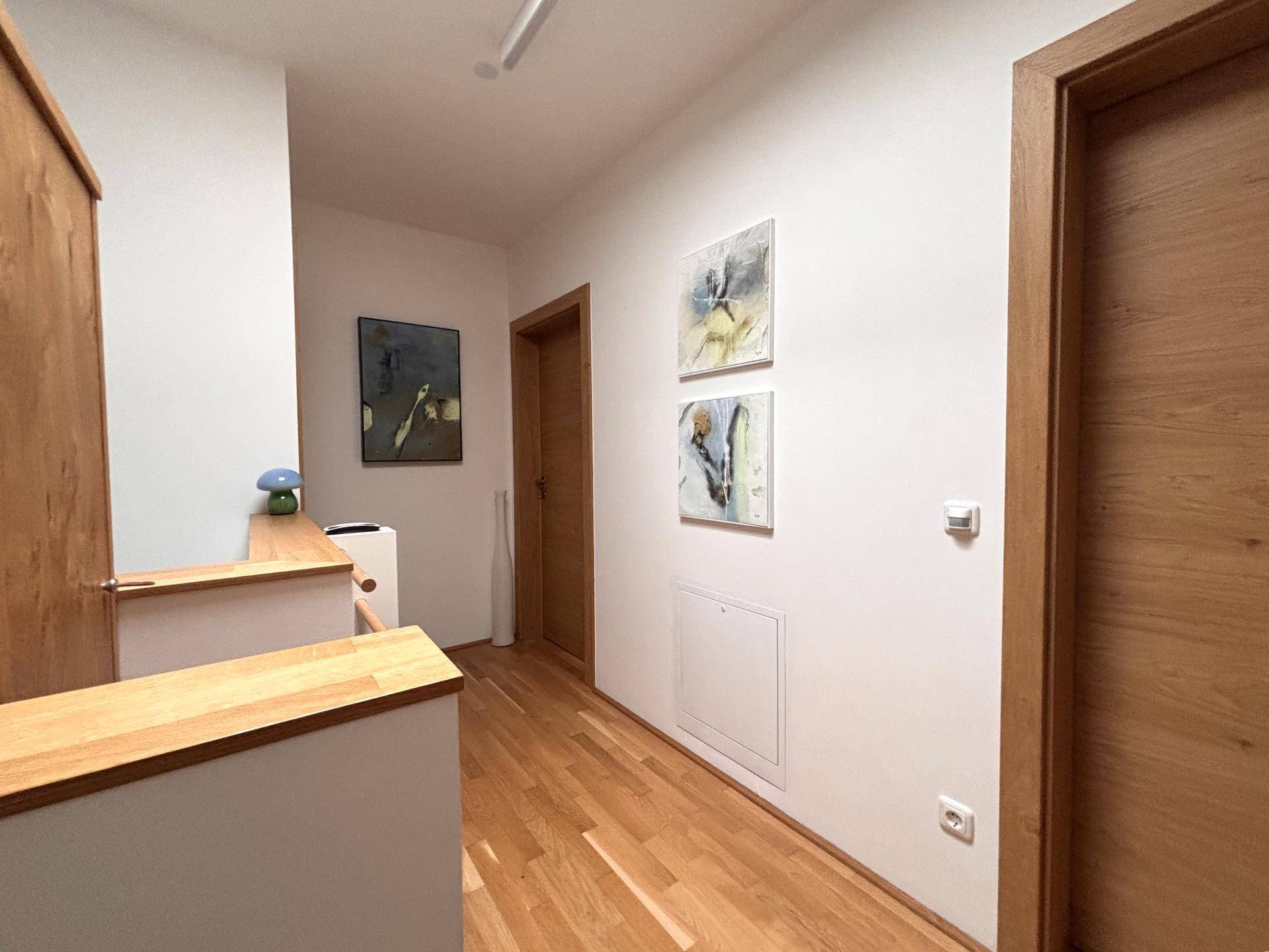 Heller Flur im Obergeschoss mit Holzgeländer, Kunstwerken und Parkettboden.