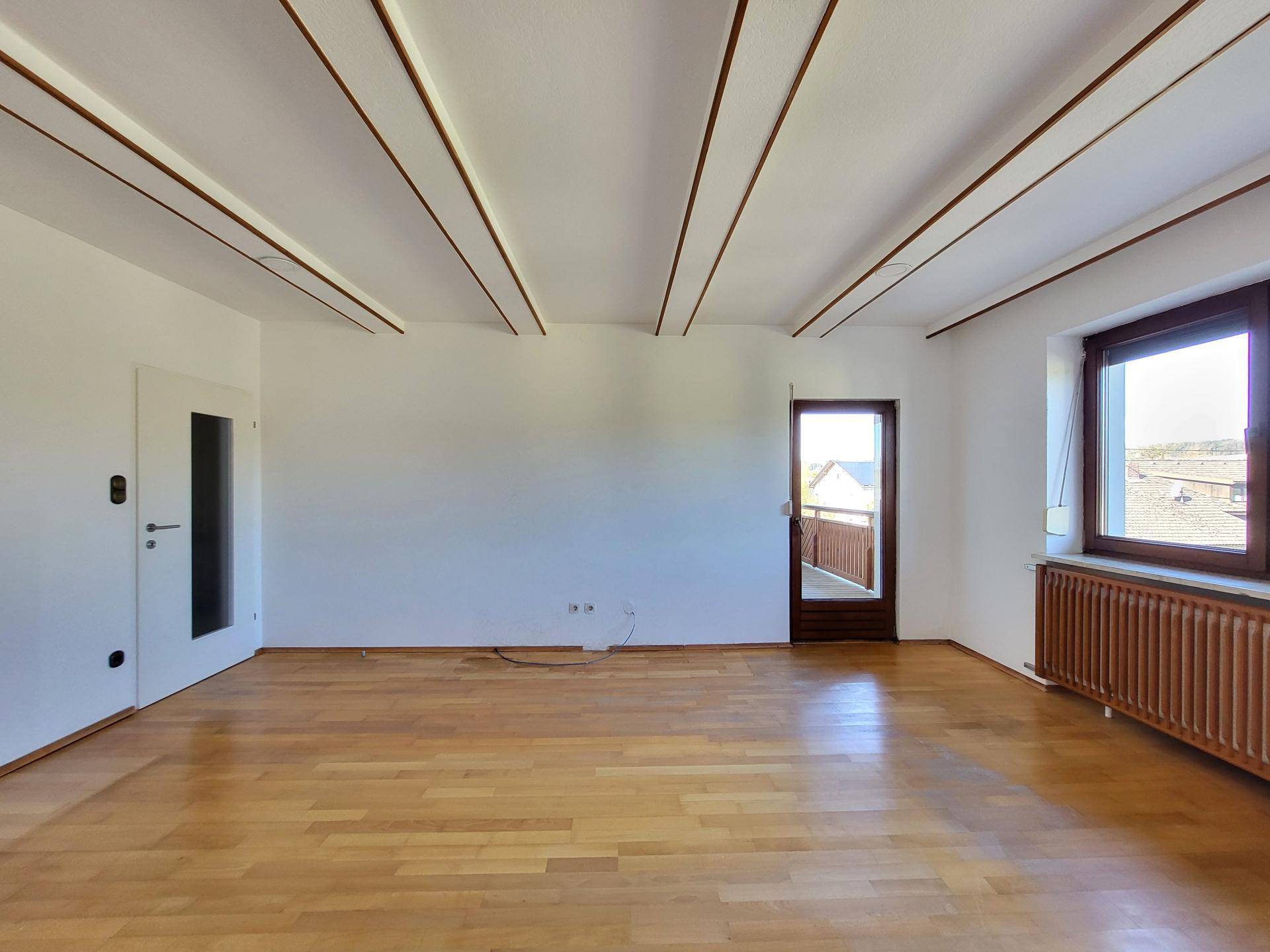 Geräumiges Wohnzimmer mit Parkettboden, Holzbalken und viel Tageslicht durch große Fenster.