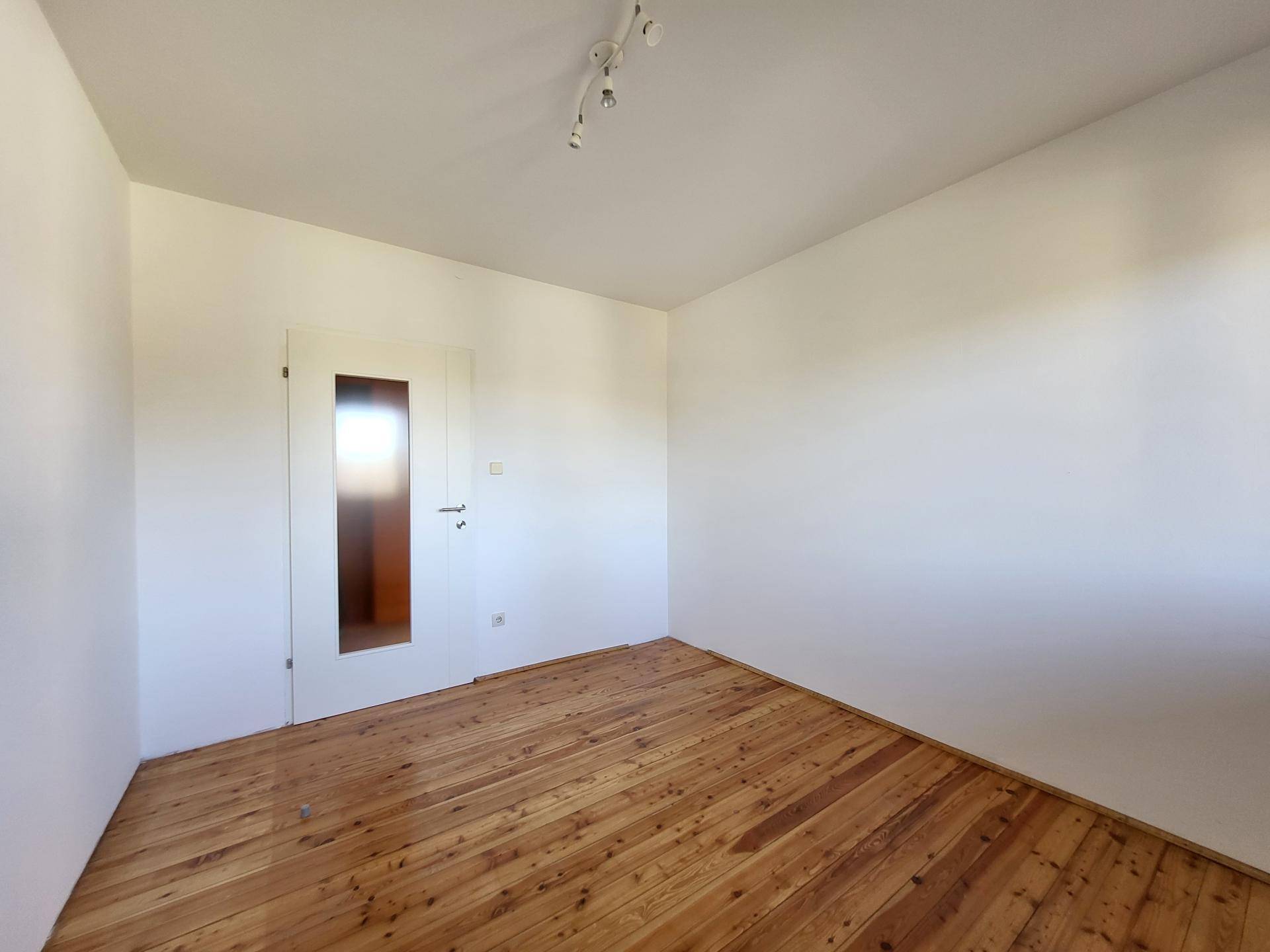 Geräumiges Zimmer mit Holzdielenboden und weiß gestrichenen Wänden.