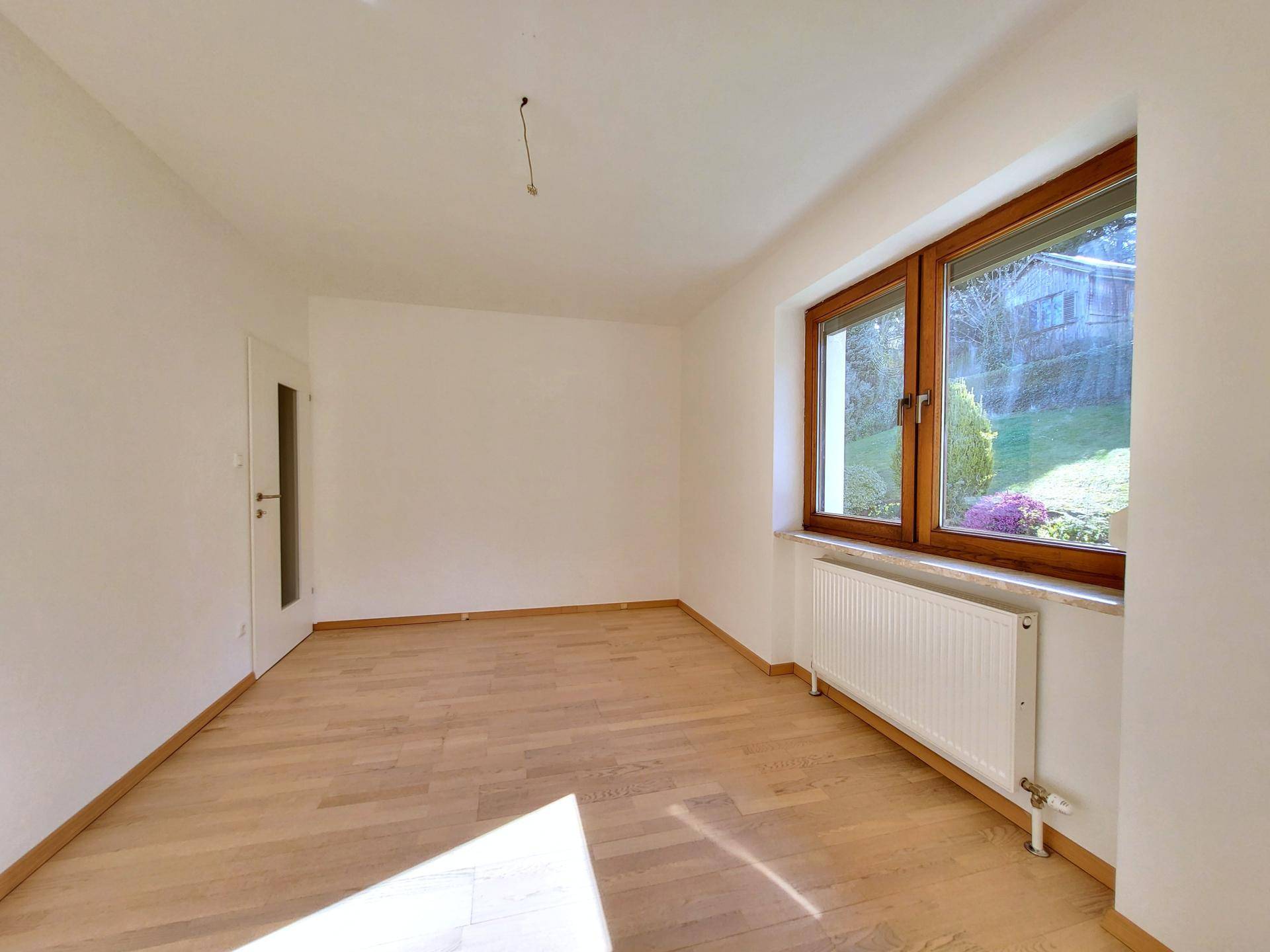 Heller Raum mit Holzboden und Fenster zum Garten, geeignet als Kinder- oder Gästezimmer.