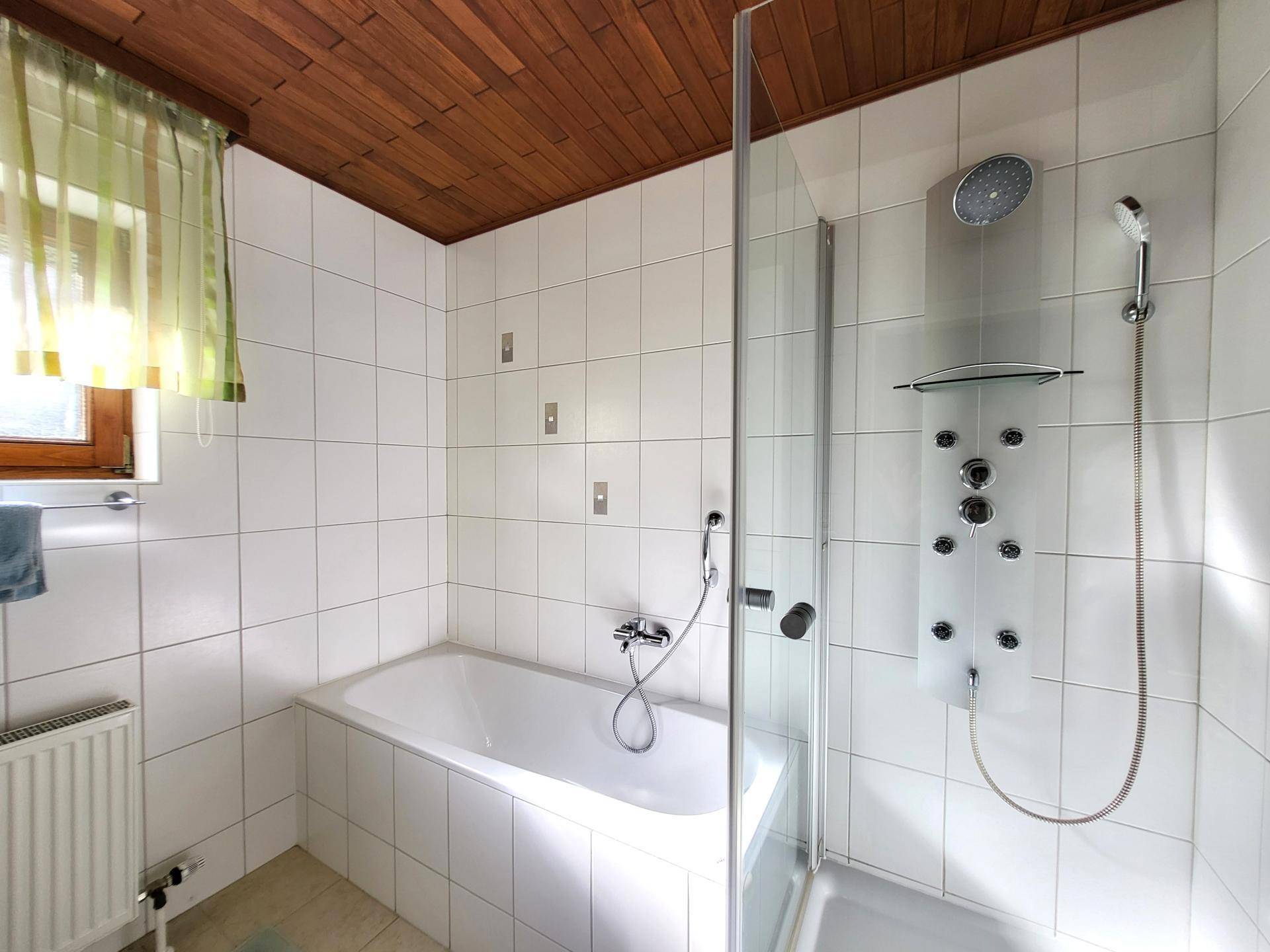 Gefliestes Badezimmer mit Badewanne, Duschkabine und Holzdecke.