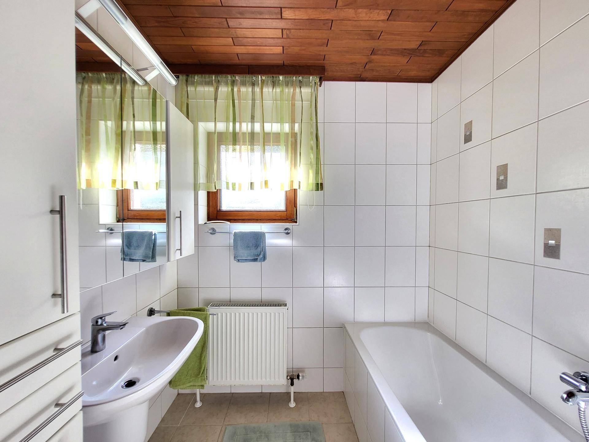Badezimmer mit Waschbecken, Spiegelschrank, Badewanne und Fenster.