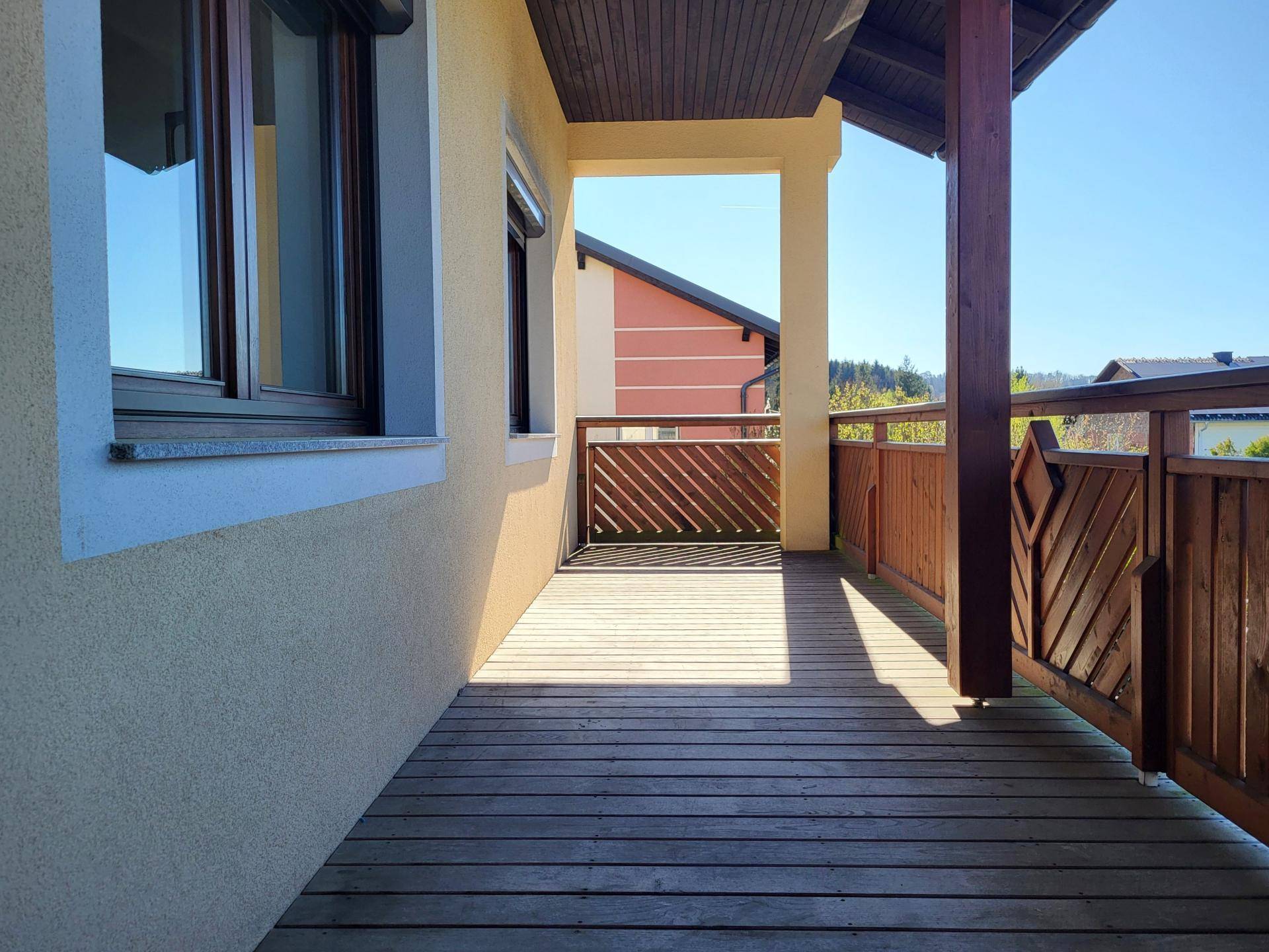 Überdachter Holzbalkon mit Geländer und Blick auf die Umgebung.