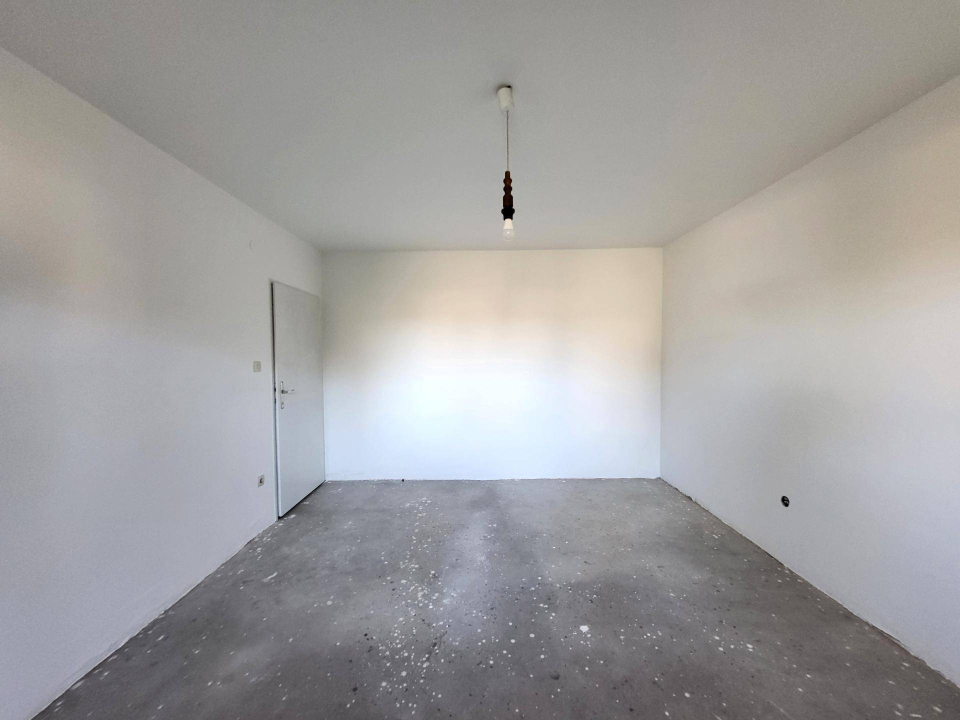 Geräumiges Zimmer mit weiß gestrichenen Wänden und Betonboden.