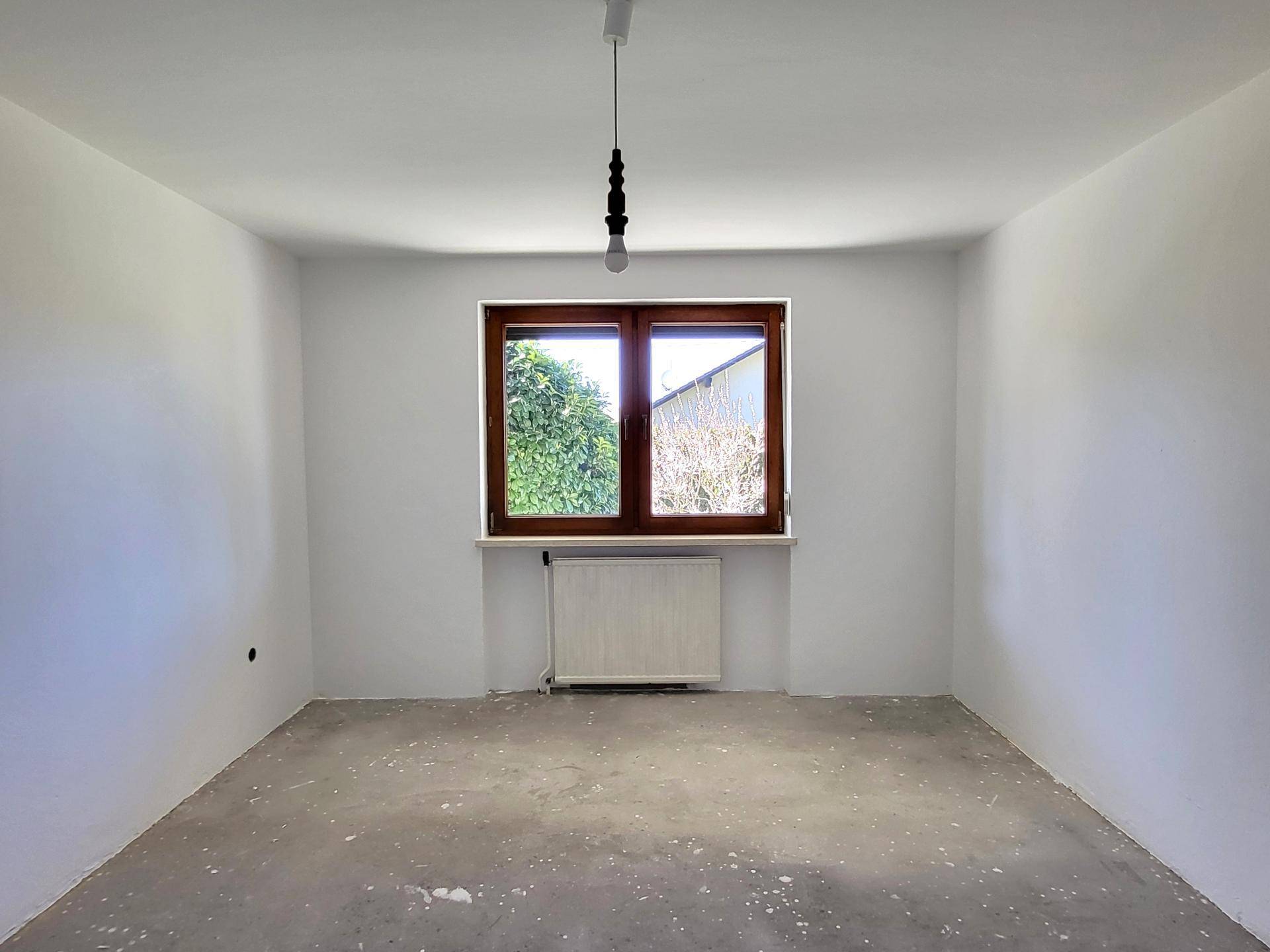 Leeres Zimmer mit Betonboden und Fenster, bereit für neue Bodenbeläge.