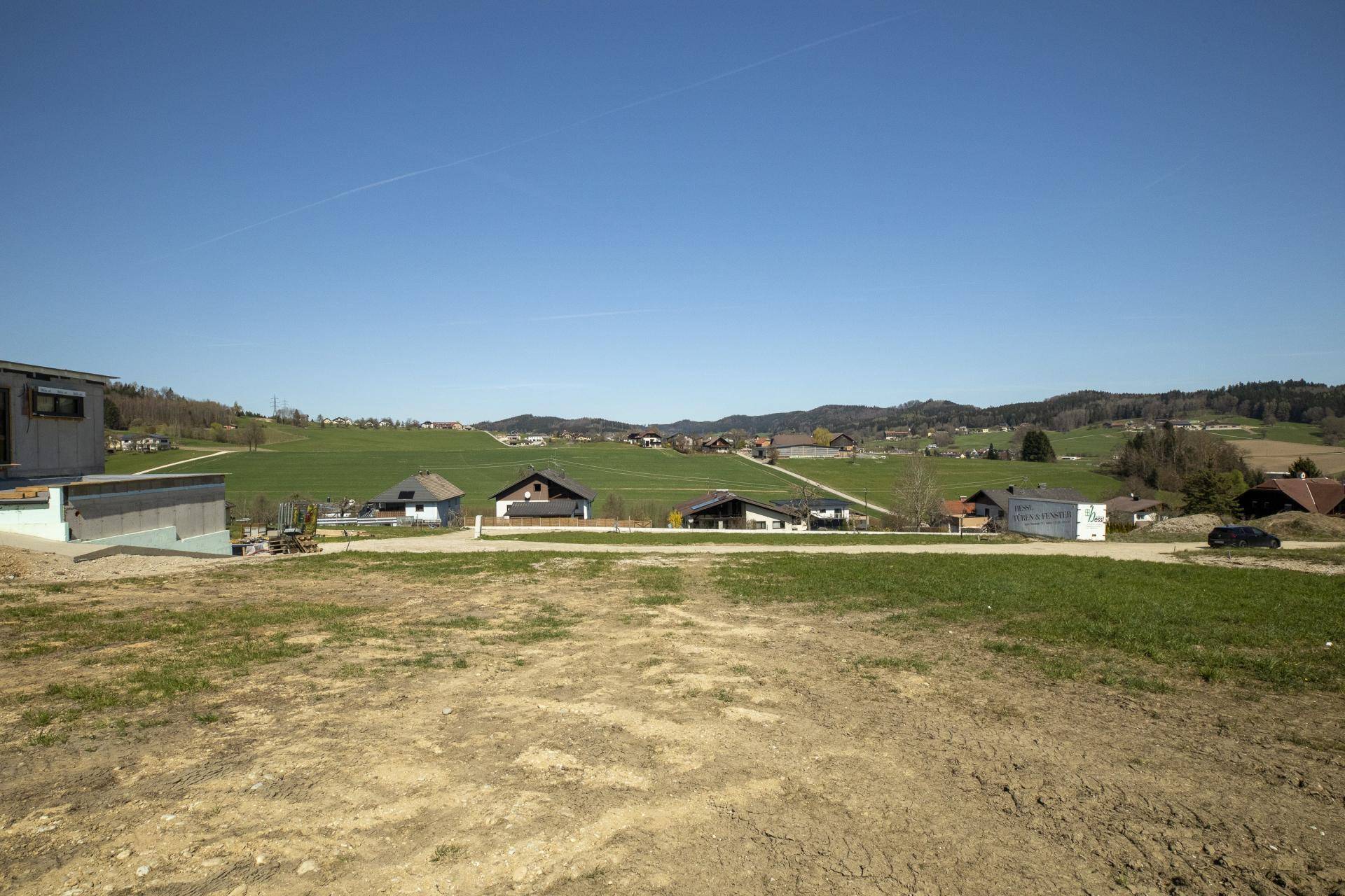 Weitläufiges Baugrundstück mit Blick auf die ländliche Umgebung und ein im Bau befindliches Gebäude.
