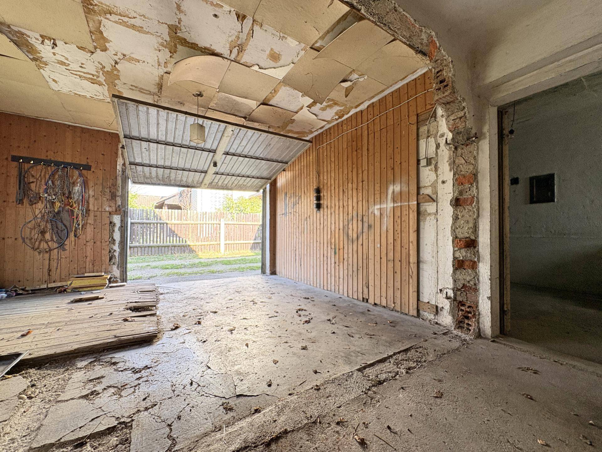 Innenansicht einer Garage mit Holzwänden und Betonboden, die Renovierung benötigt.
