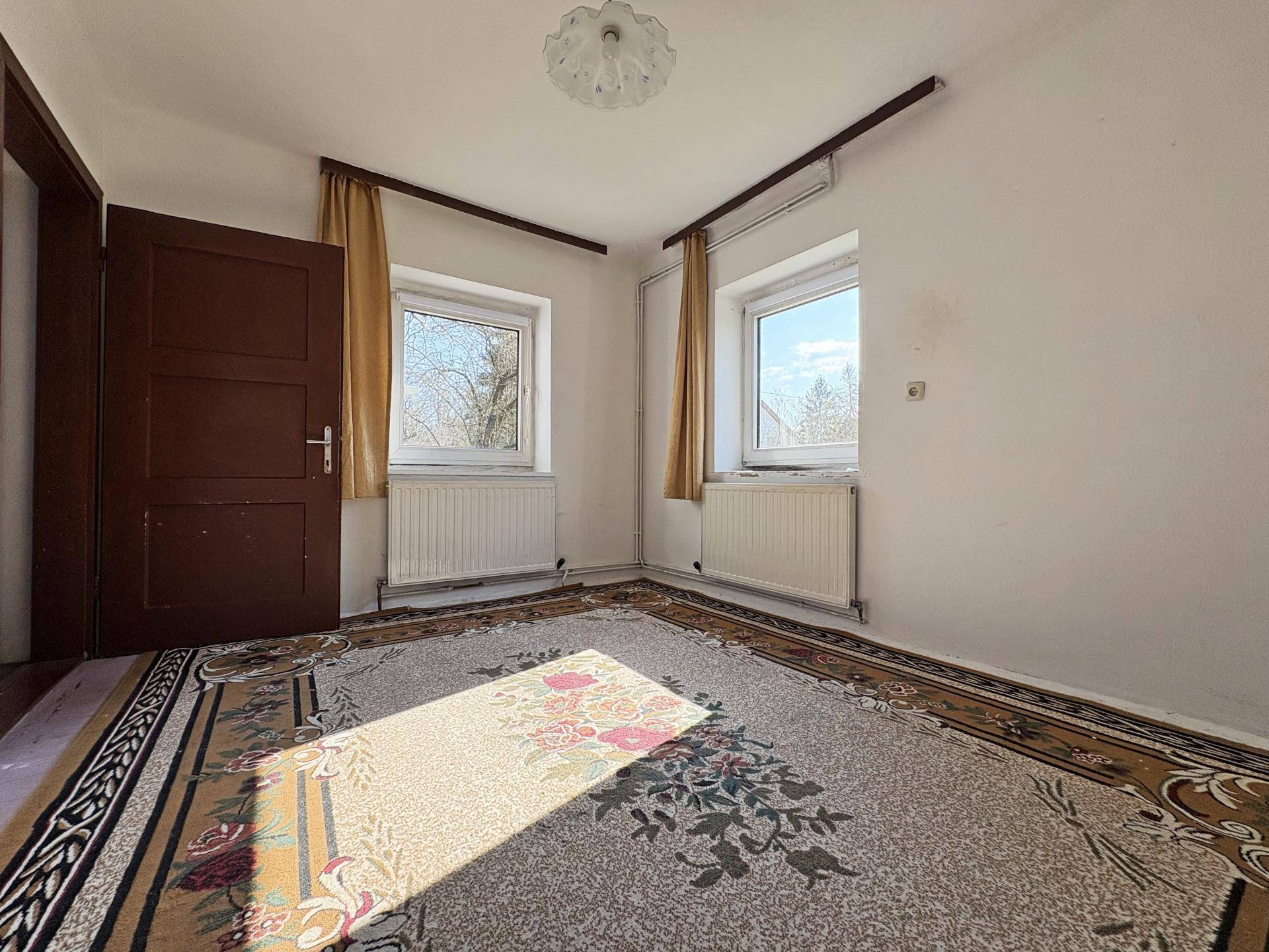 Schlafzimmer mit Teppichboden, zwei Fenstern und viel Tageslicht, dekoriert mit einem bunten Teppich.