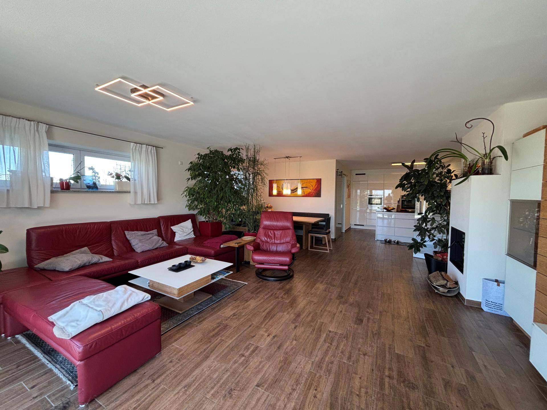 Geräumiger offener Wohn-Essbereich mit rotem Sofa, Holzboden und vielen Pflanzen, hell und einladend.