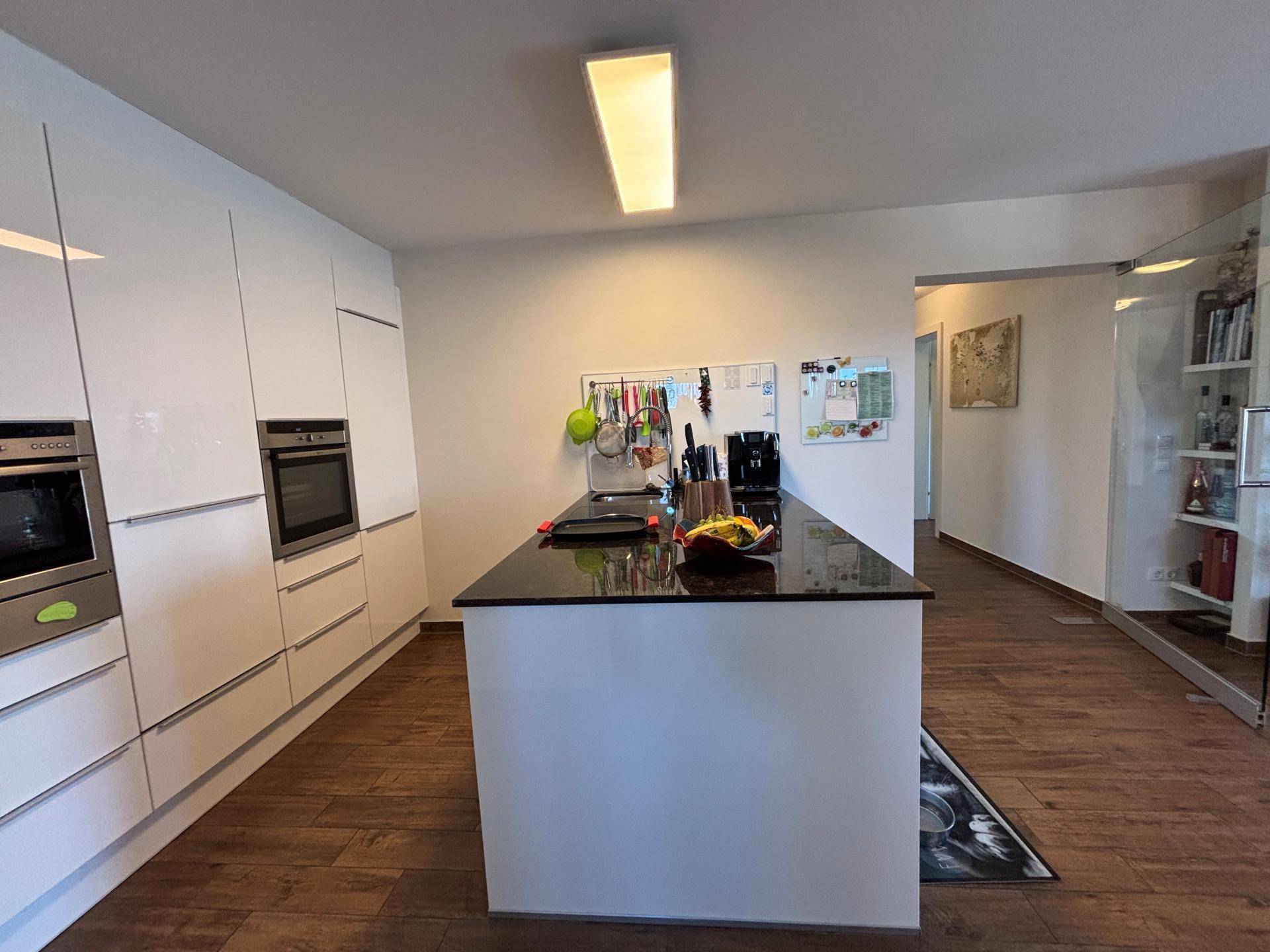 Moderne weiße Küche mit Hochglanzfronten, Kücheninsel und integrierten Geräten, offen gestaltet.
