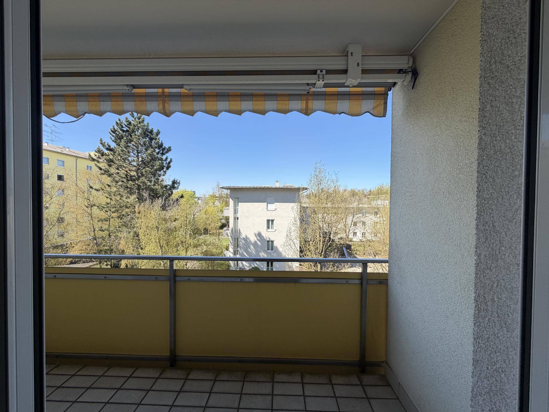 Balkon mit Markise und Blick auf die umliegenden Gebäude und Bäume.