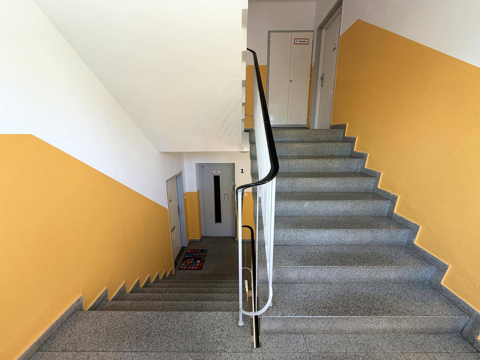 Treppenhaus mit gelb gestrichenen Wänden und Granitstufen, inklusive Zugang zum Aufzug.