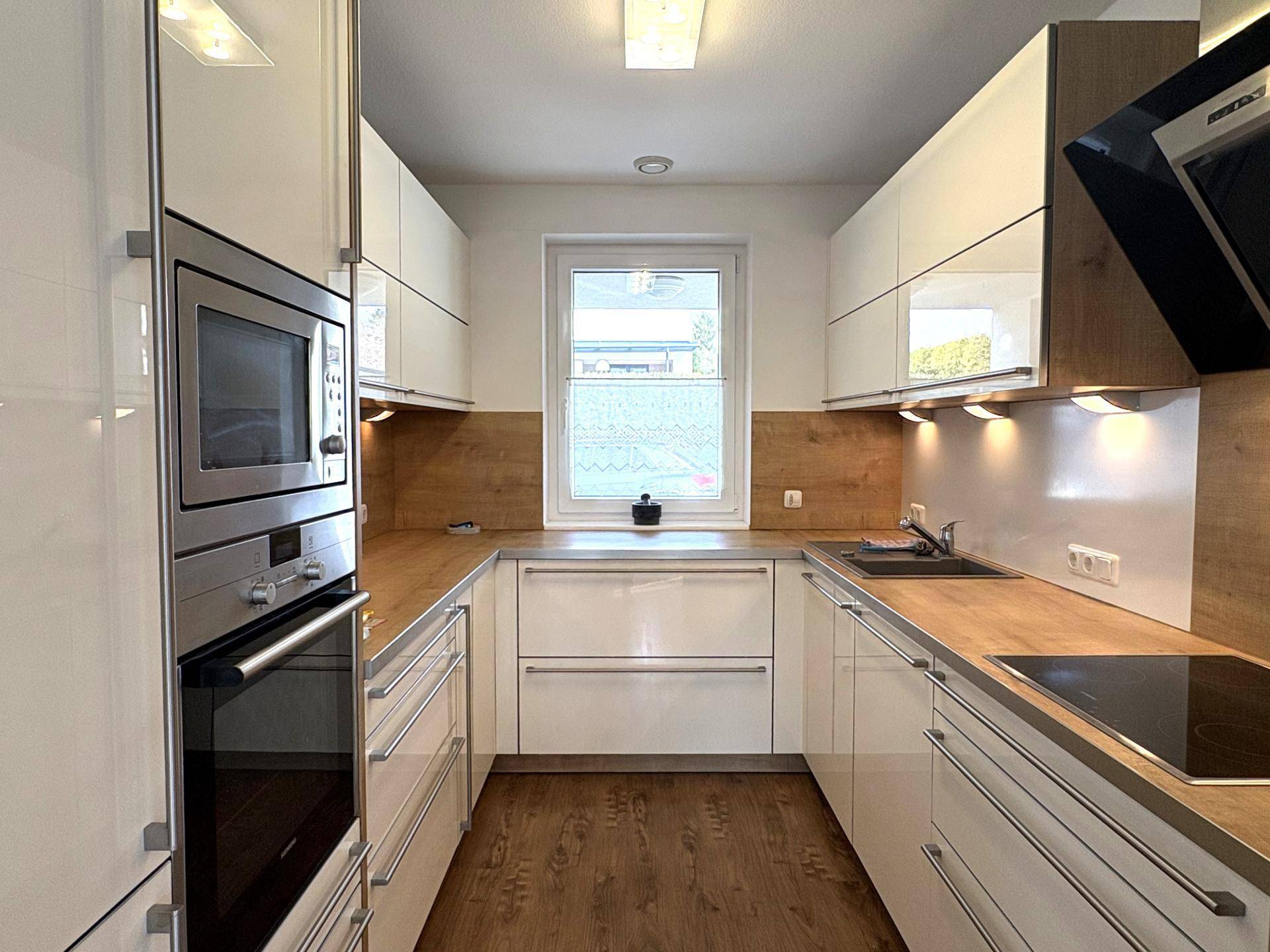 Moderne Einbauküche mit weißen Hochglanzfronten, Holz-Arbeitsplatten und integrierten Geräten.