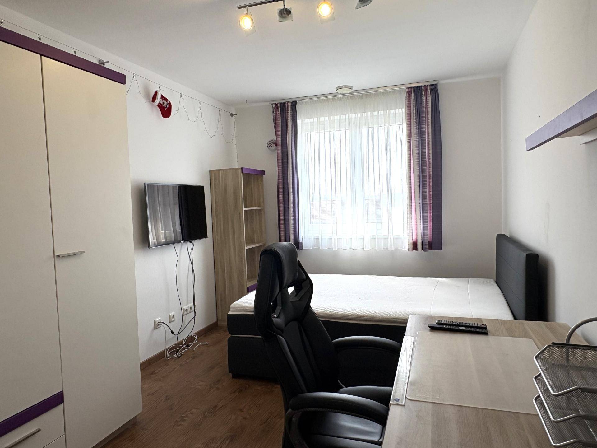 Schlafzimmer mit Bett, Schreibtisch und Fenster, ausgestattet mit Laminatboden.