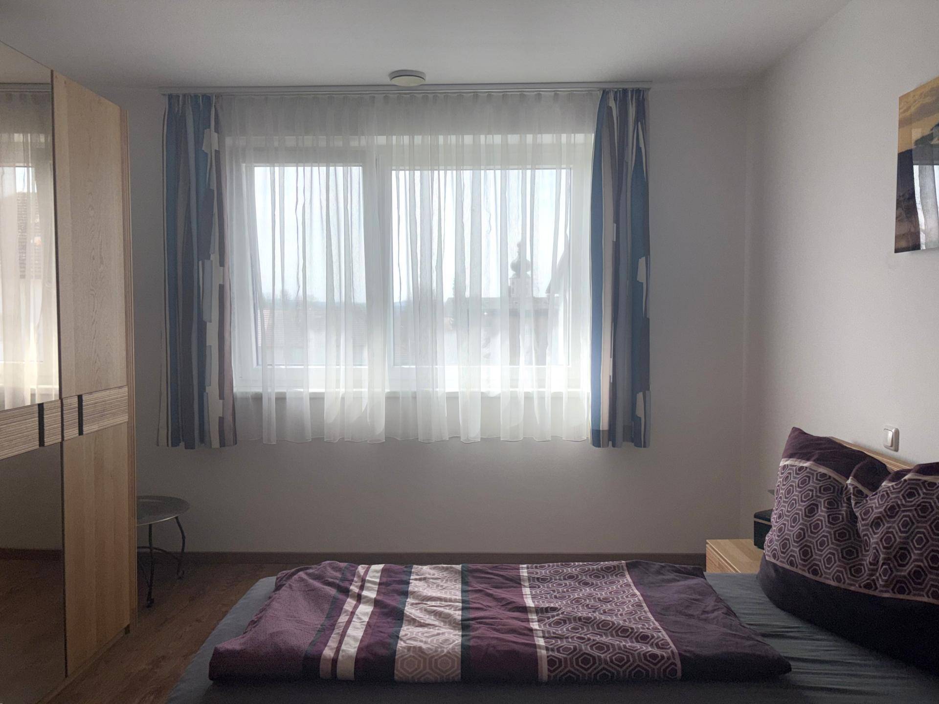 Helles Schlafzimmer mit großem Fenster und gemütlichem Bett.