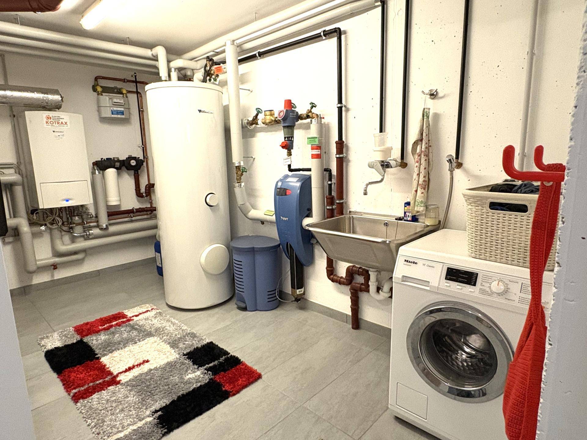 Heizungsraum im Keller mit Waschmaschine, Warmwasserspeicher und Fliesenboden.