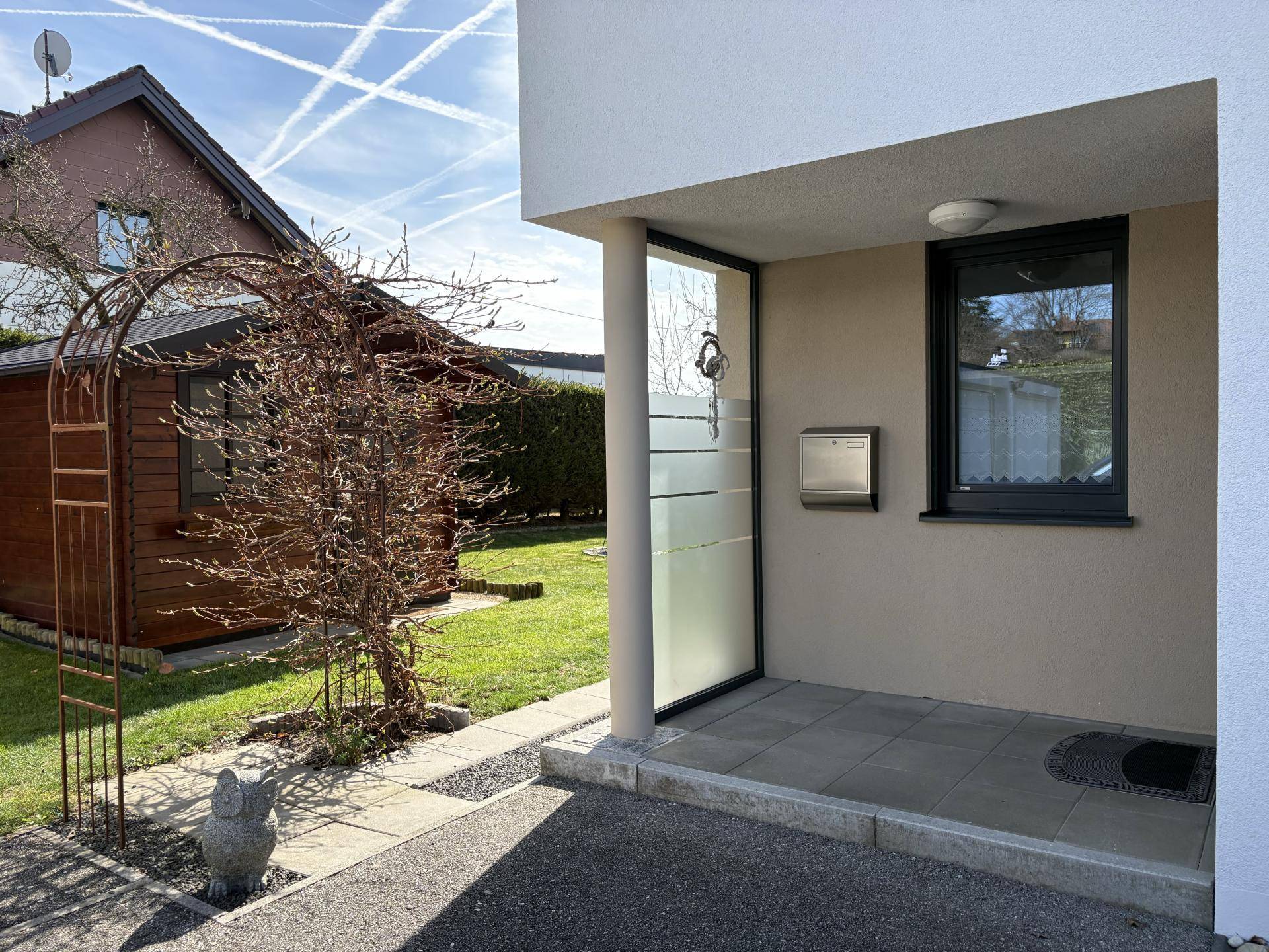 Eingangsbereich des Hauses mit moderner Haustür, Briefkasten und gepflastertem Zugang.