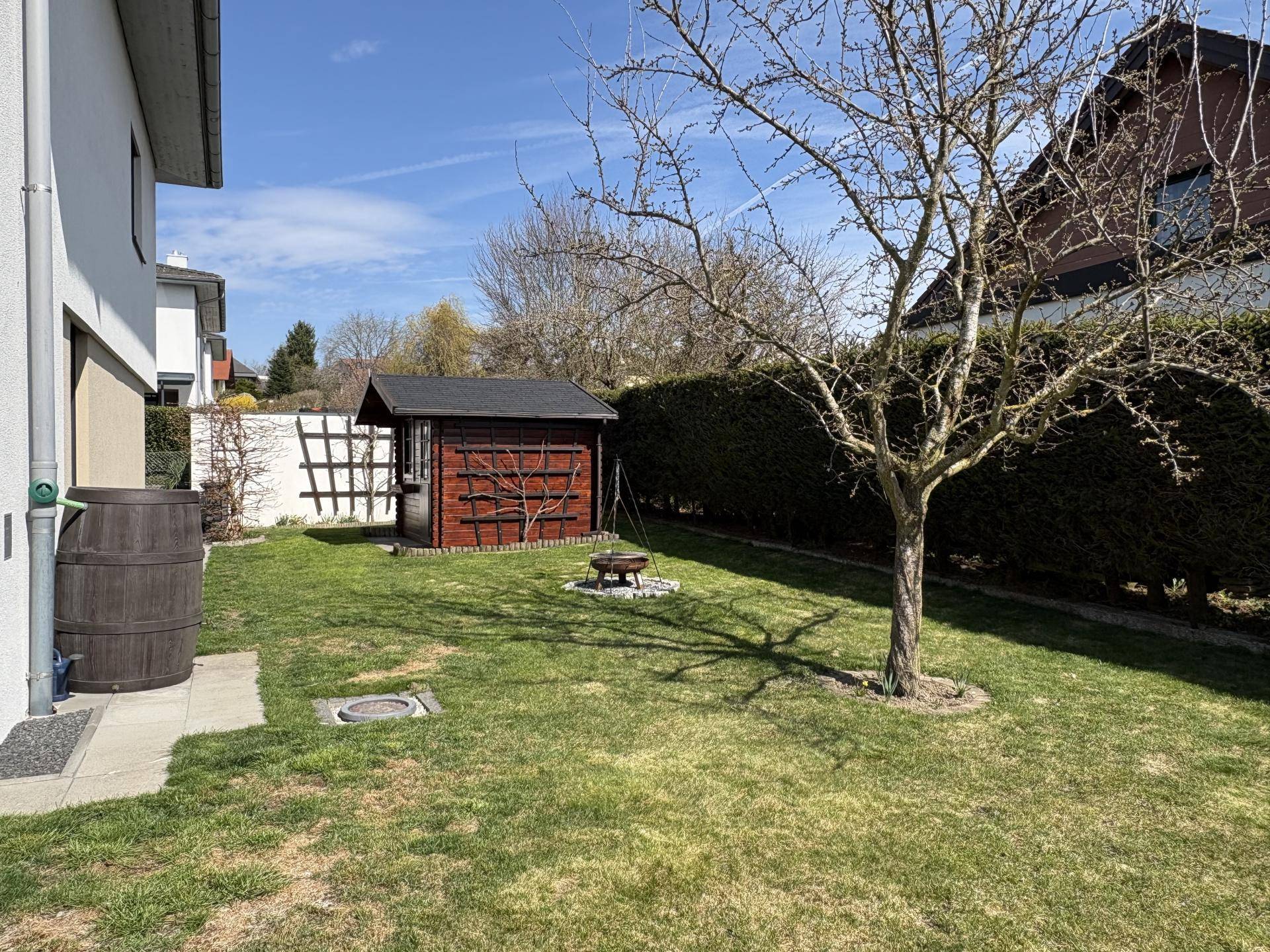 Gartenbereich mit Rasenfläche, Gartenhaus, Feuerstelle und altem Baum.