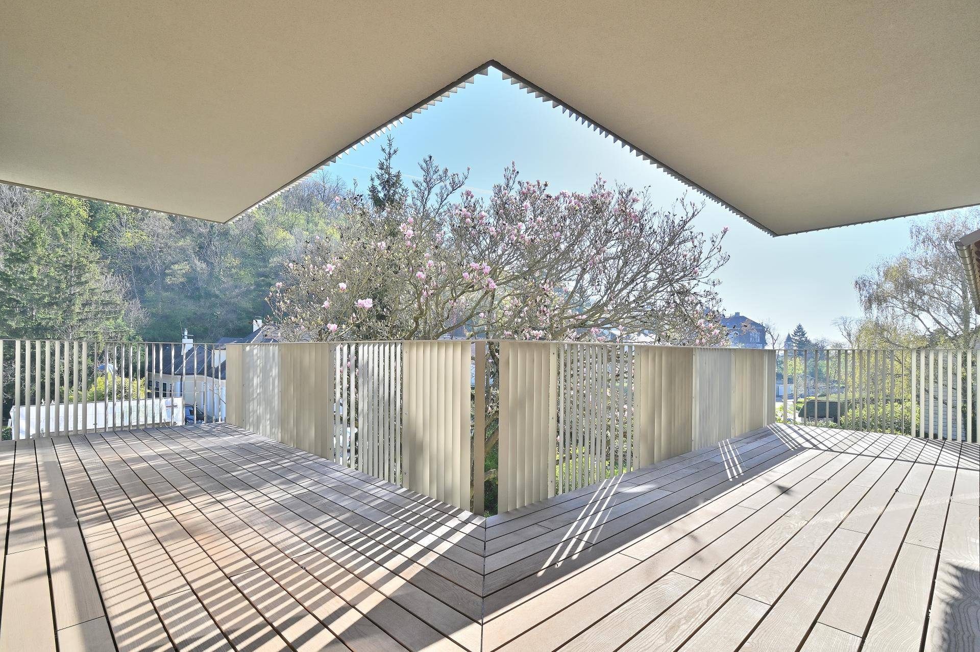 Großer, sonniger Balkon mit Holzdielenboden und Blick auf blühende Bäume.