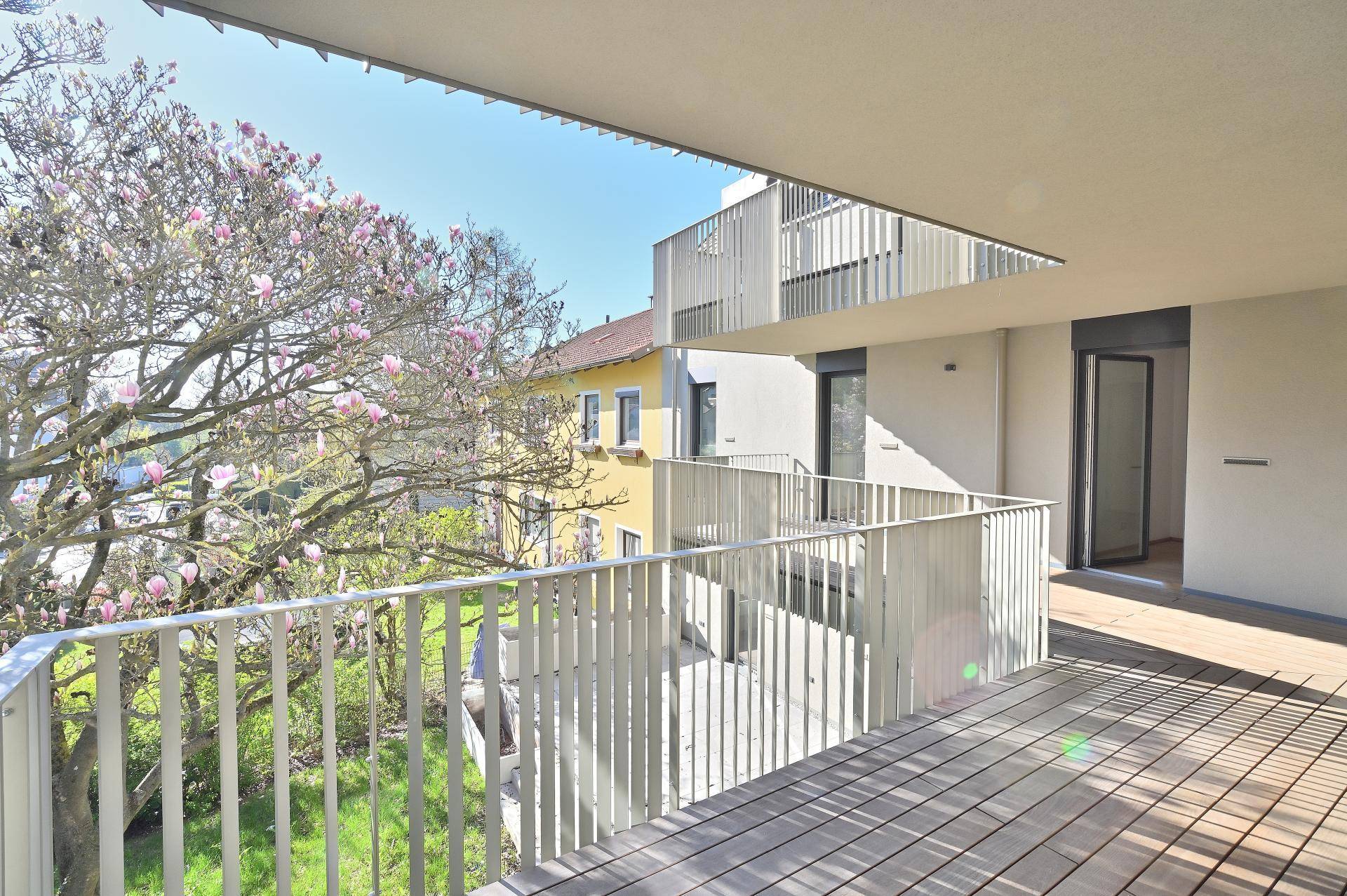 Weiter Blick vom Balkon mit Holzboden auf die Umgebung und blühende Magnolienbäume.