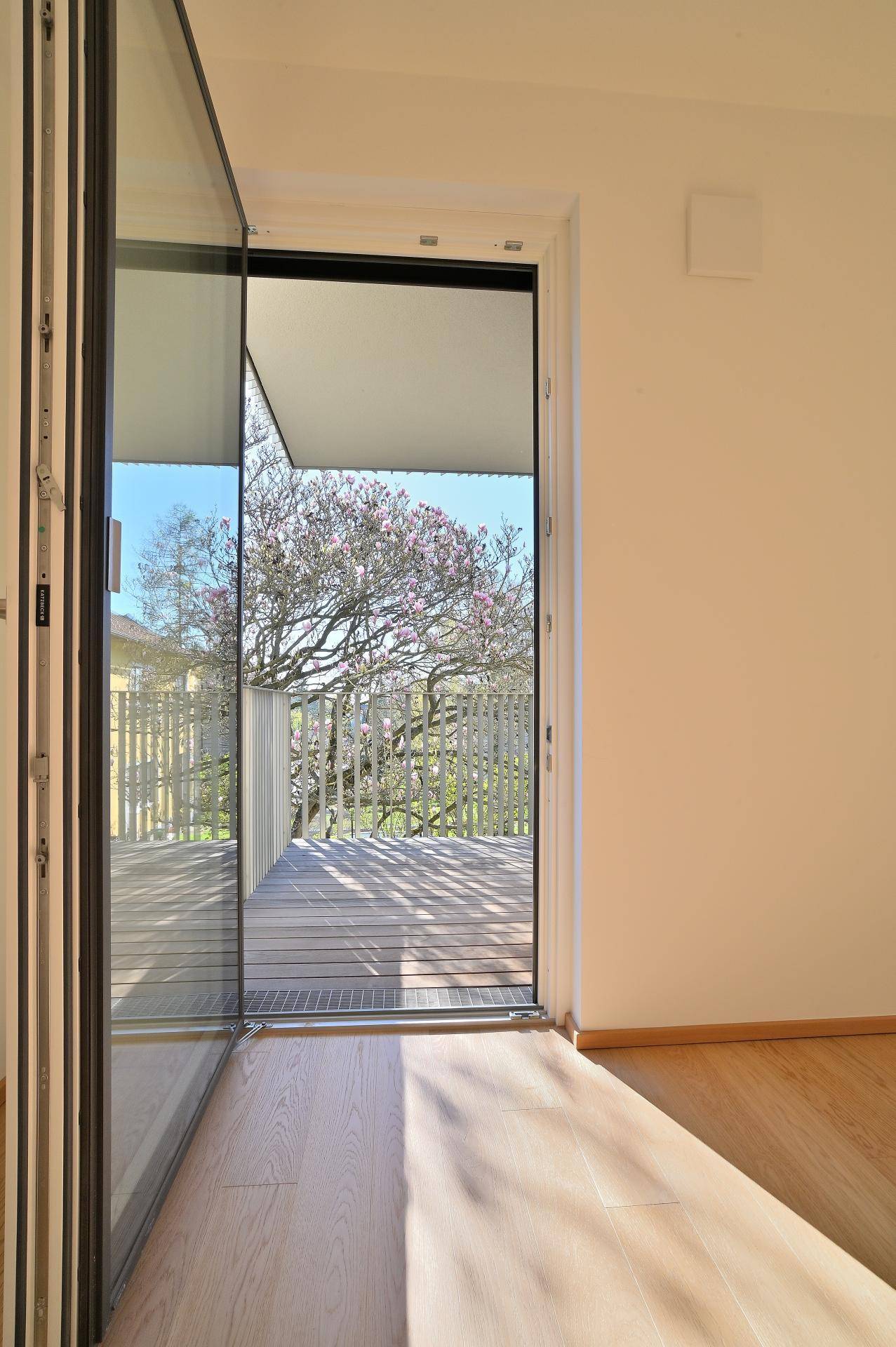 Heller Innenraum mit Zugang zum Balkon, der einen Blick auf blühende Bäume bietet.