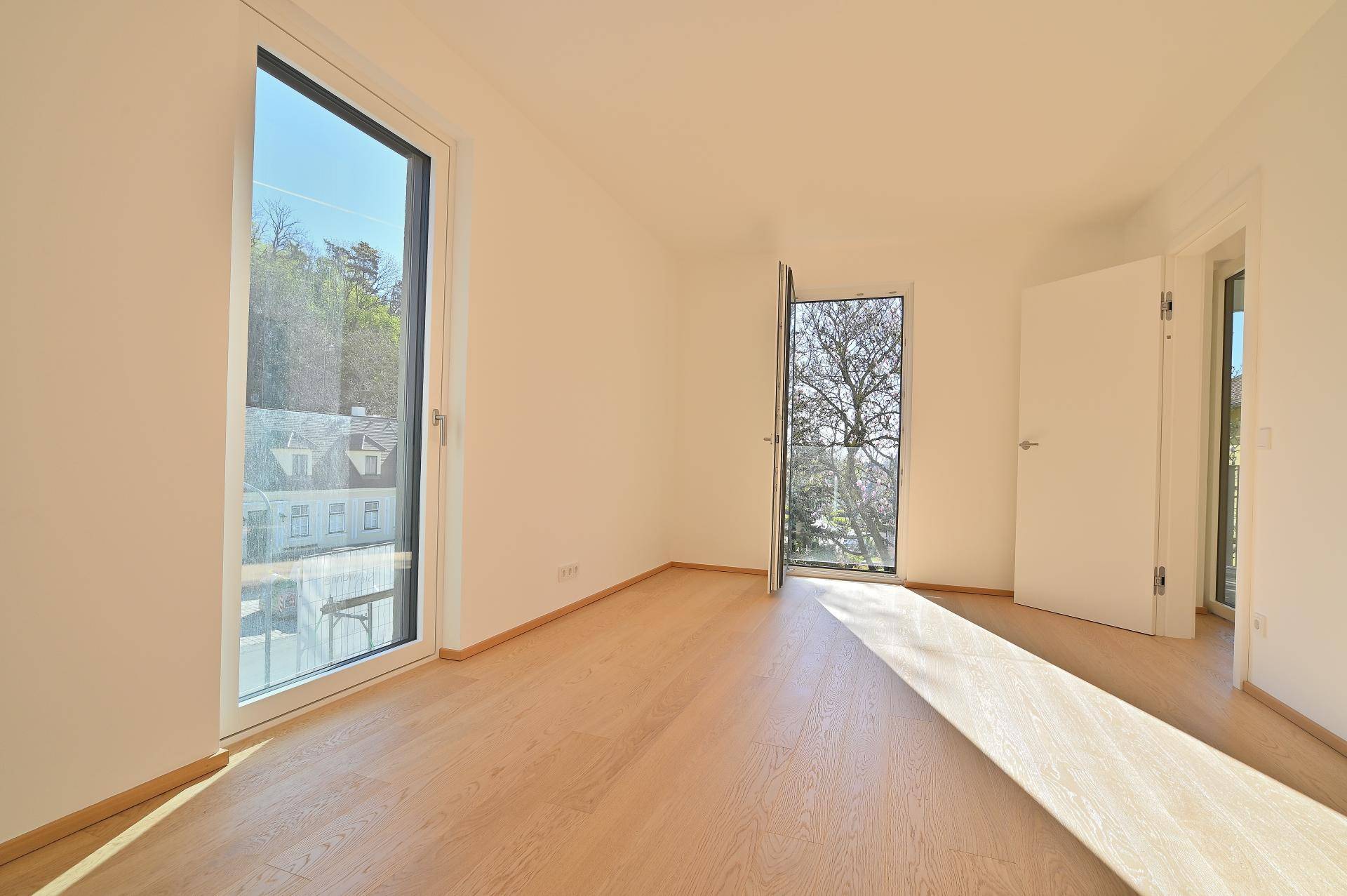 Helles Schlafzimmer mit Holzboden, großen Fenstern und Zugang zum Außenbereich.