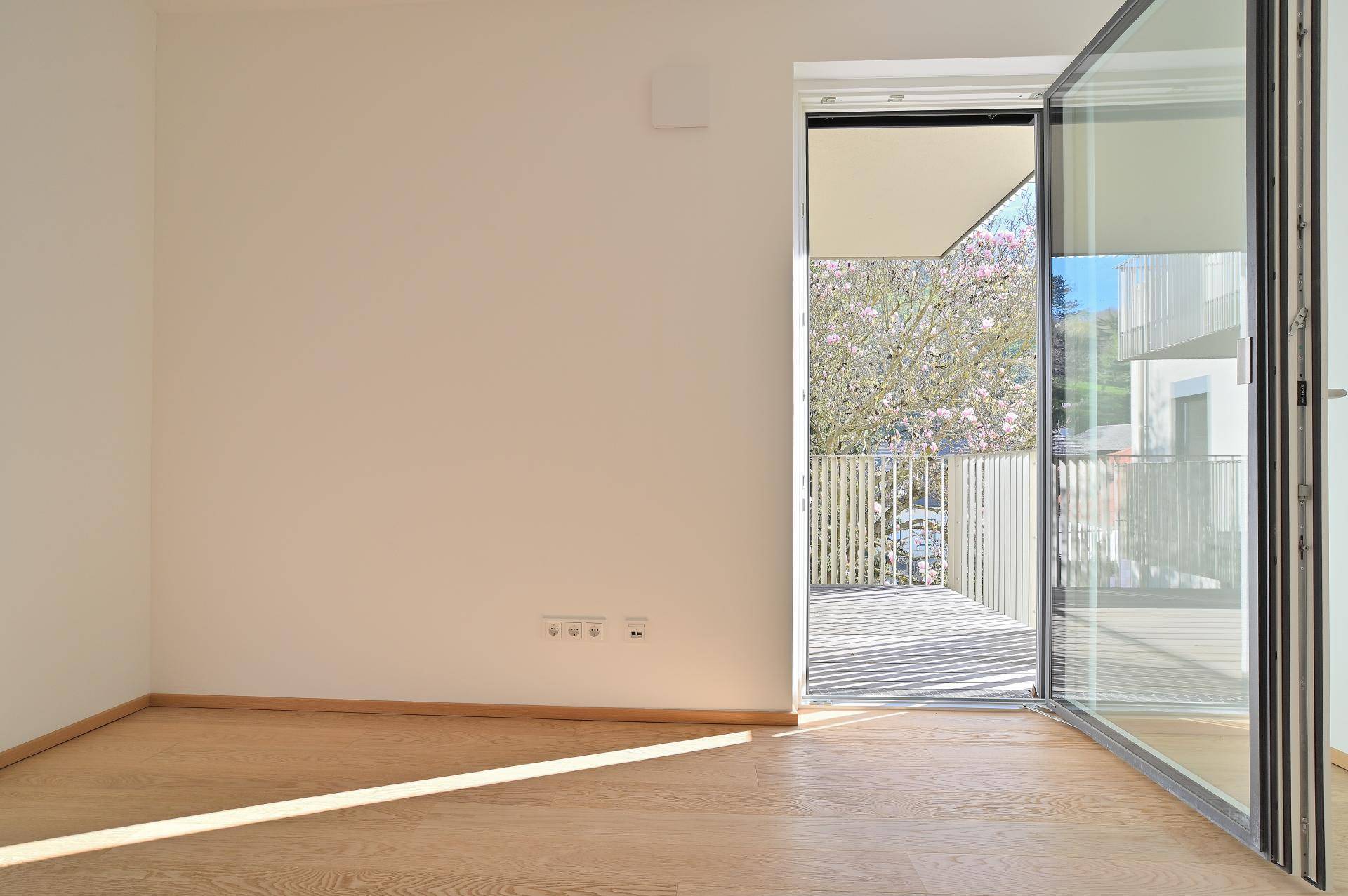 Helles Zimmer mit Holzboden und direktem Zugang zu einem sonnigen Balkon.