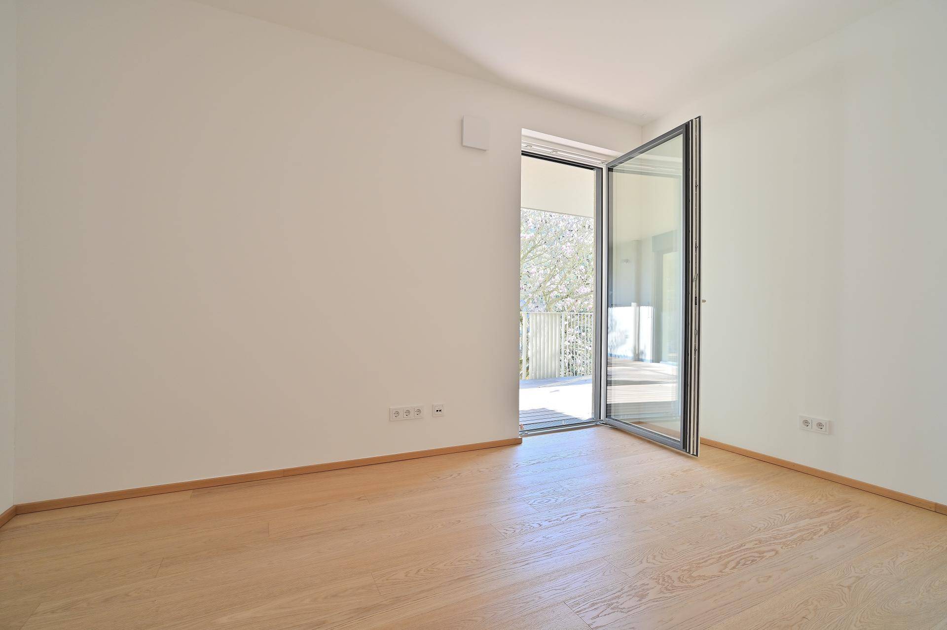 Geräumiges, helles Zimmer mit Holzboden und Zugang zu einem Außenbereich.