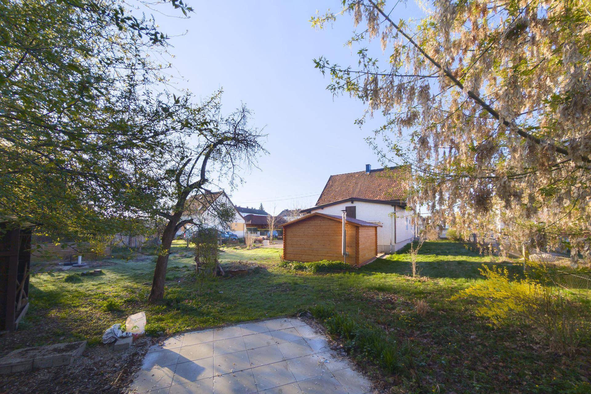 Großer Gartenbereich hinter dem Haus mit Rasenfläche, Bäumen und einem kleinen Gartenhaus.