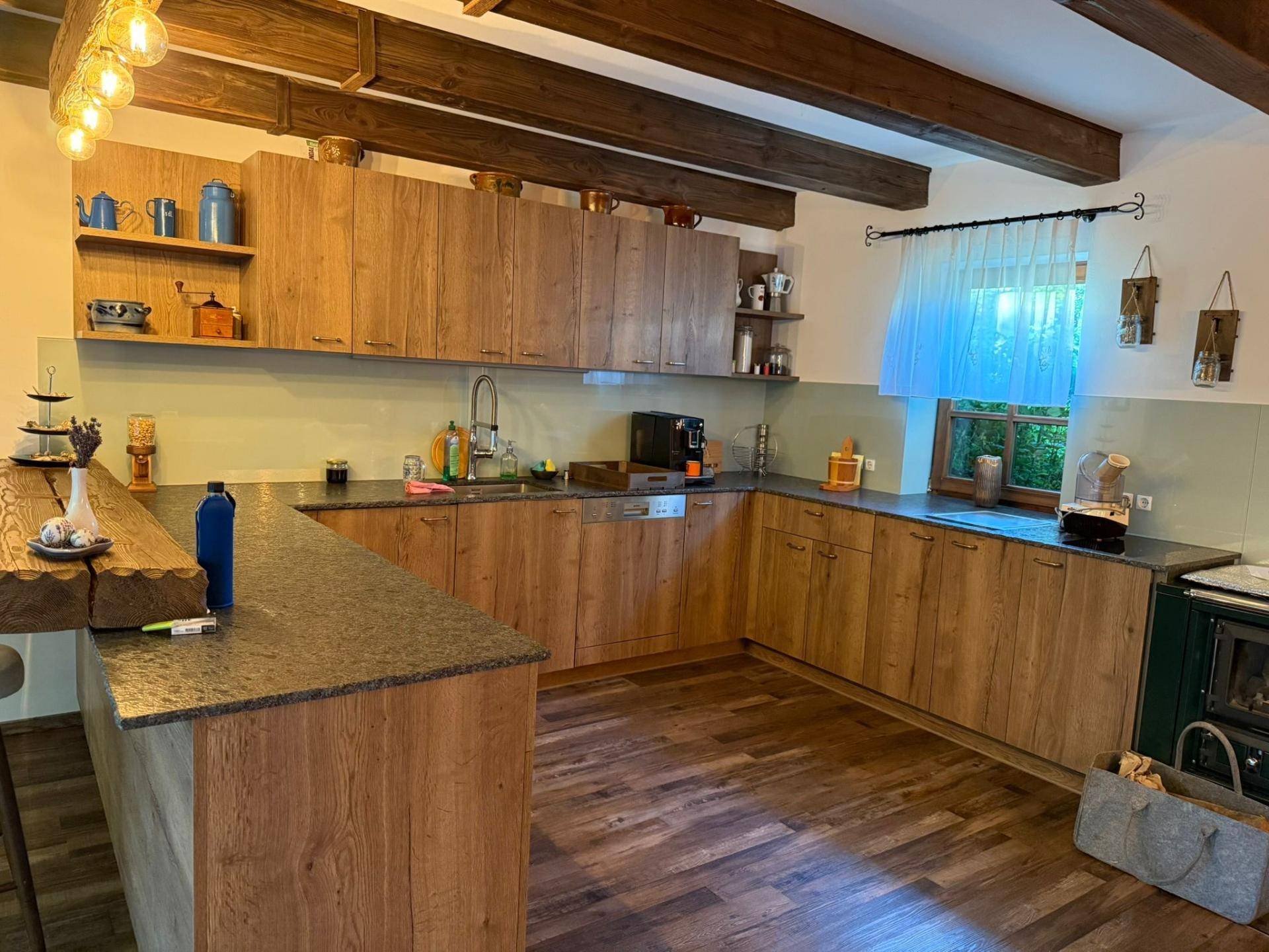 Geräumige Küche mit Holzschränken, dunkler Arbeitsplatte und integrierten Geräten.