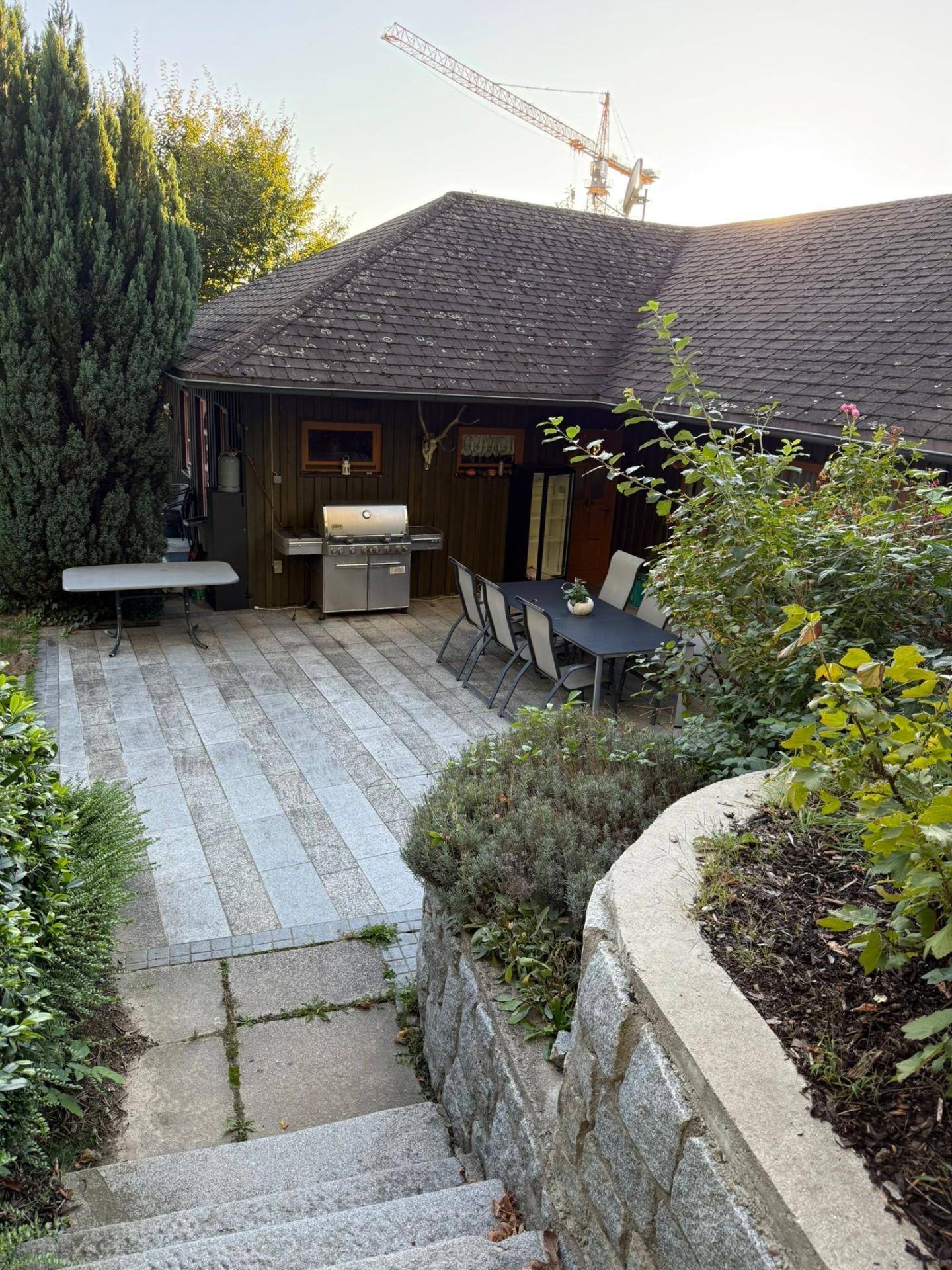 Gepflasterte Terrasse mit Grillstation und Esstisch im Freien, umgeben von Grün.