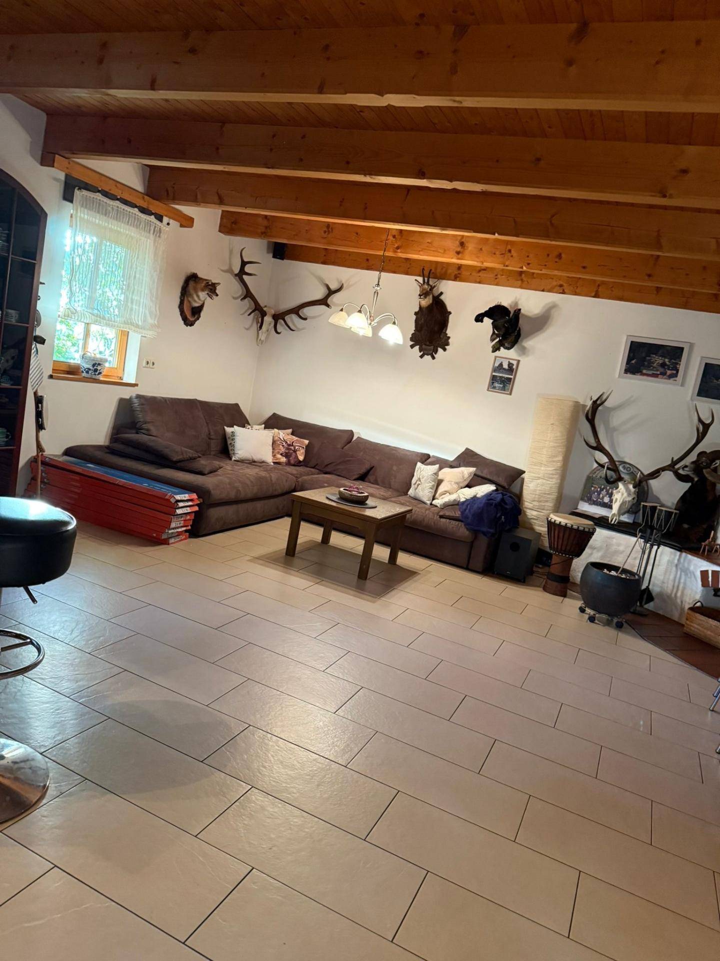 Geräumiges Wohnzimmer mit hellen Fliesen, sichtbaren Holzbalken und großem Ecksofa.
