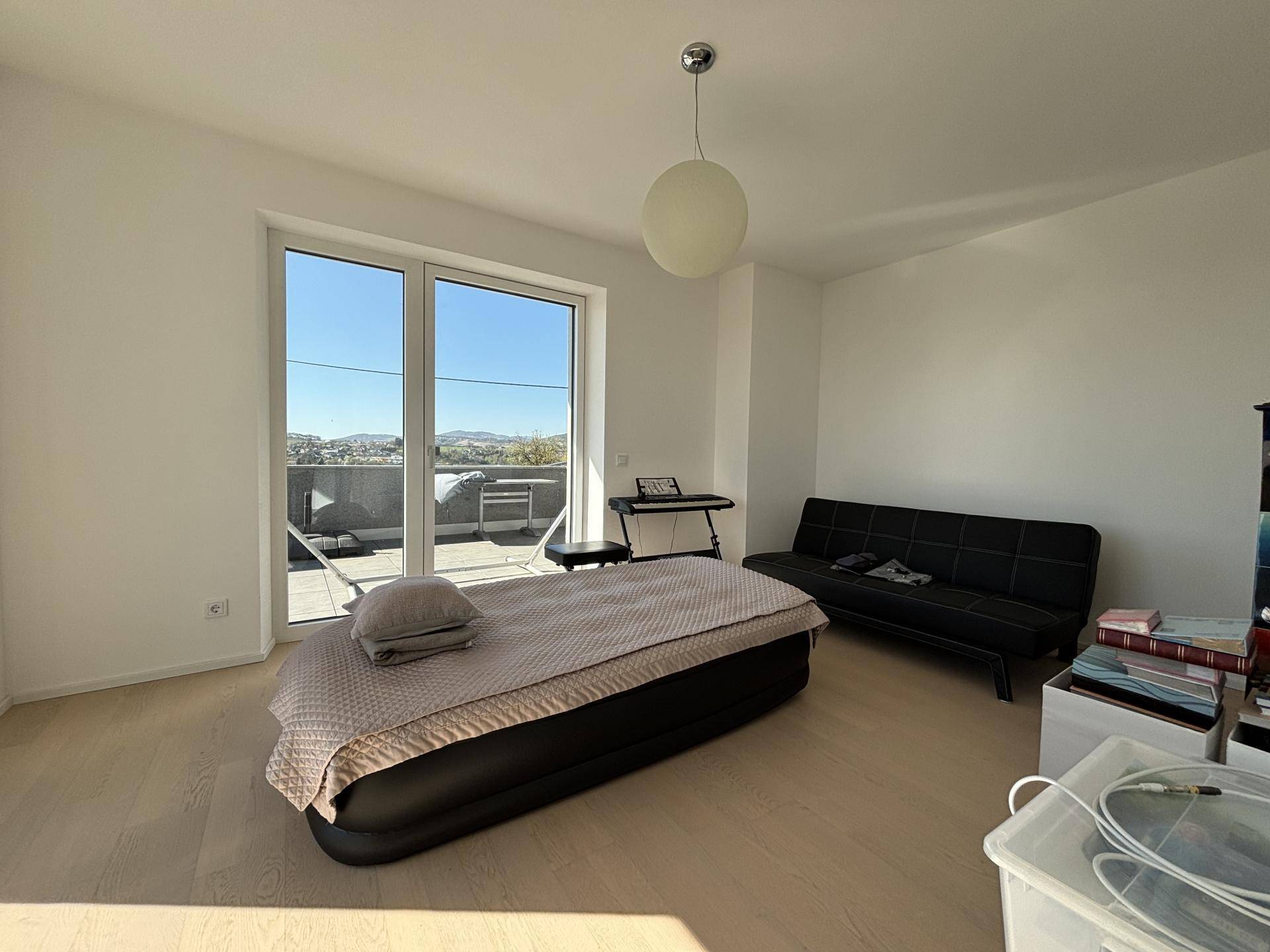 Helles Schlafzimmer mit Zugang zu einer Terrasse und Blick auf die Umgebung, ausgestattet mit einem Sofa.