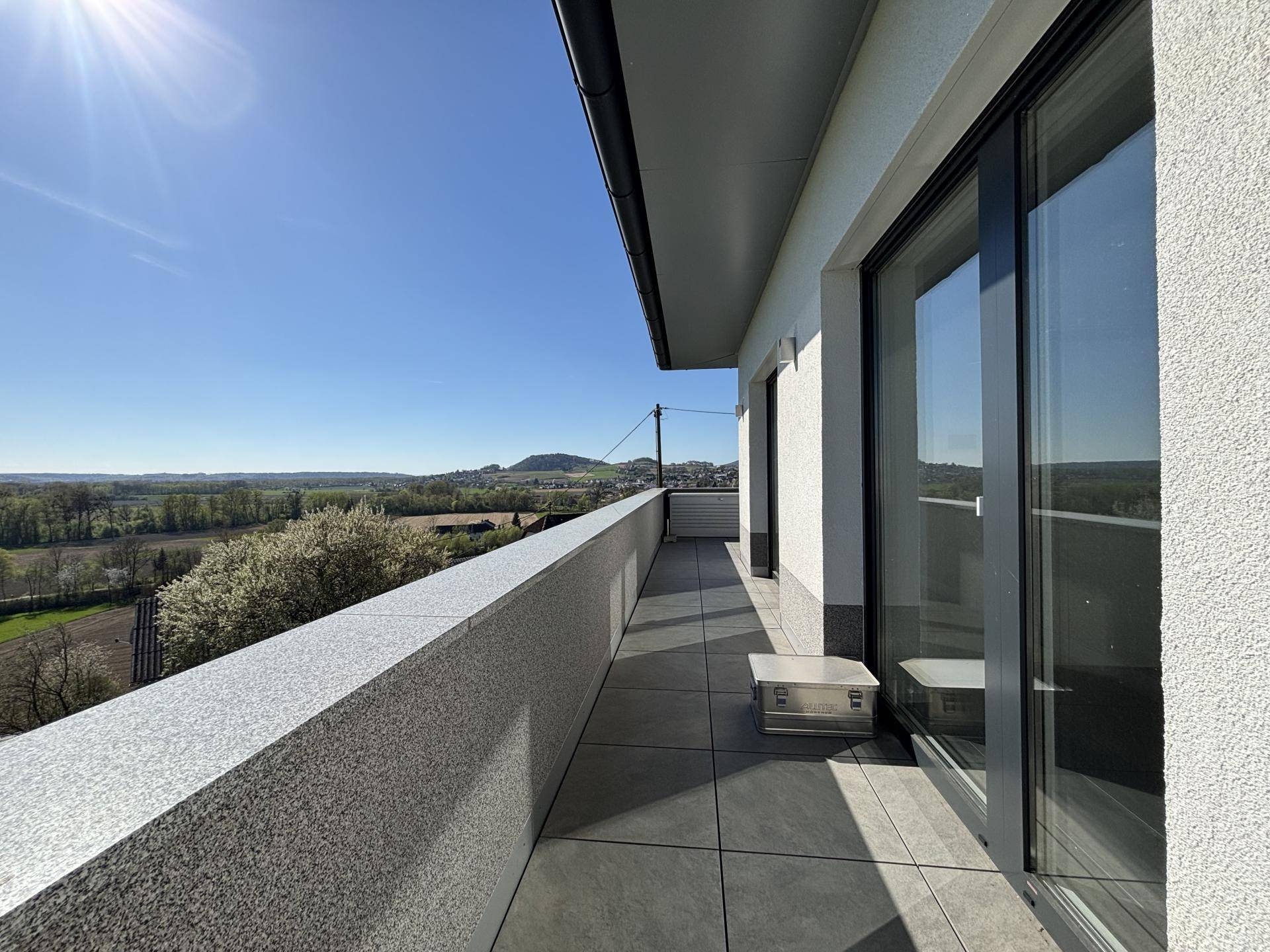 Langer Balkon mit weitem Blick über die grüne Landschaft und ferne Berge an einem sonnigen Tag.