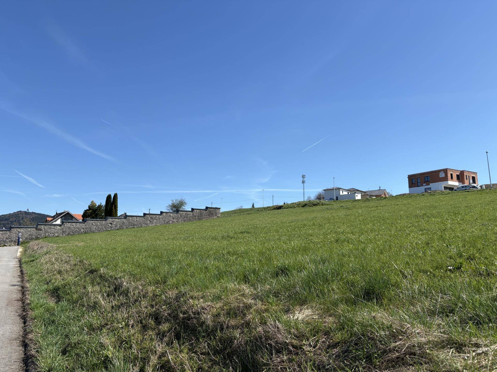 Grüne Hügellandschaft mit einem Pfad im Vordergrund und vereinzelten Häusern am Horizont unter blauem Himmel.