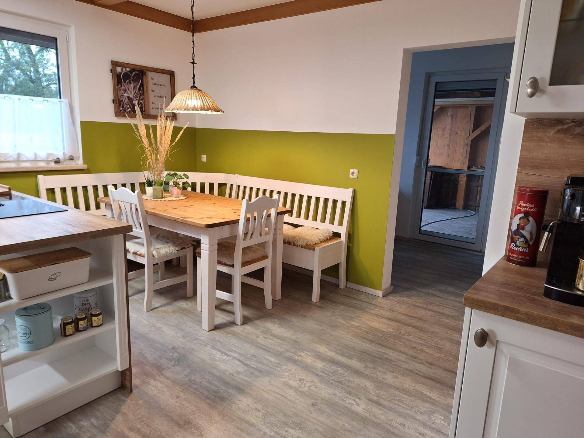 Essbereich in der Küche mit Holztisch, Eckbank und grüner Akzentwand.
