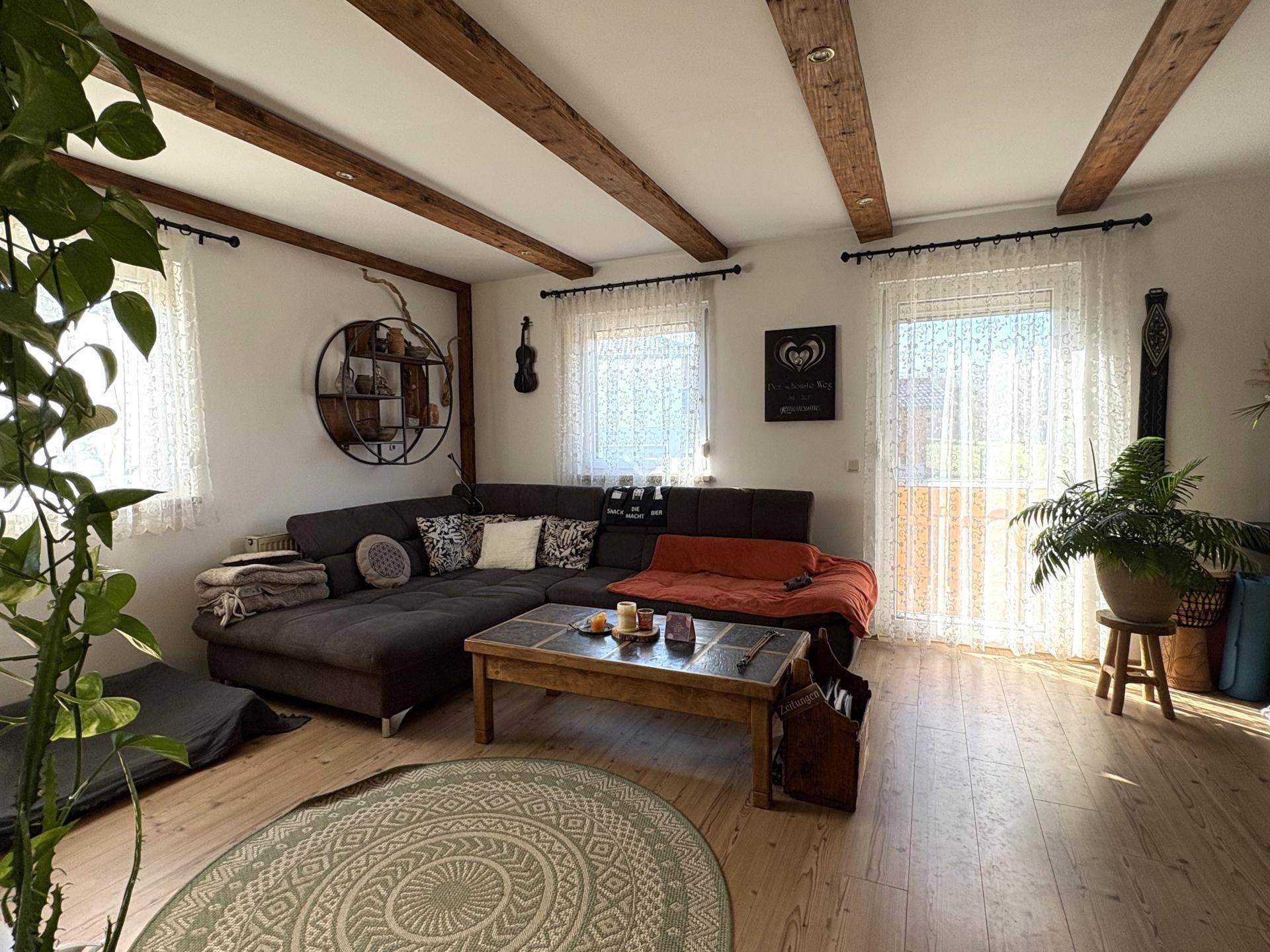 Gemütliches Wohnzimmer mit großem Ecksofa, Holzboden und Zugang zum Balkon.