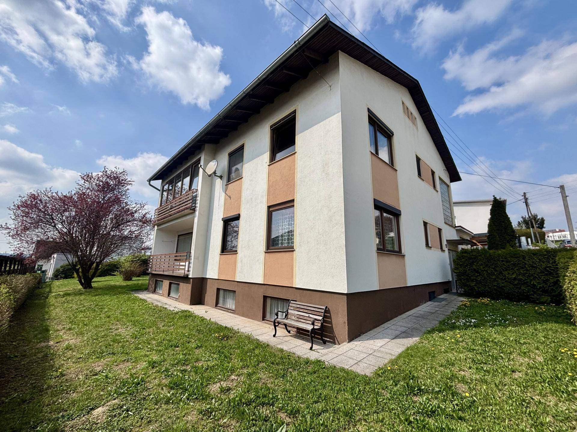 Hausansicht von der Seite mit Garten, Sitzbank und Zugang zum weitläufigen Grundstück.
