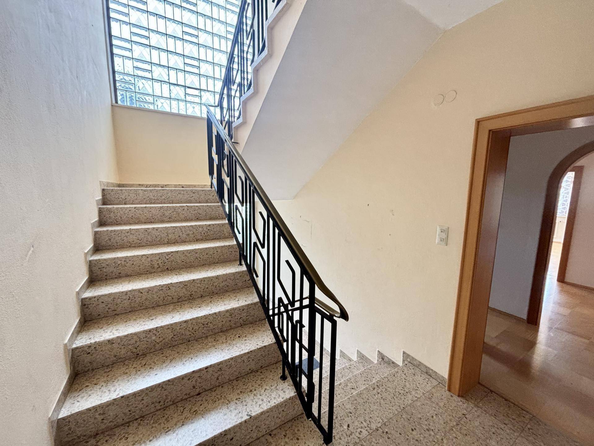 Treppenhaus mit Terrazzoboden und schmiedeeisernem Geländer, das die Etagen verbindet.