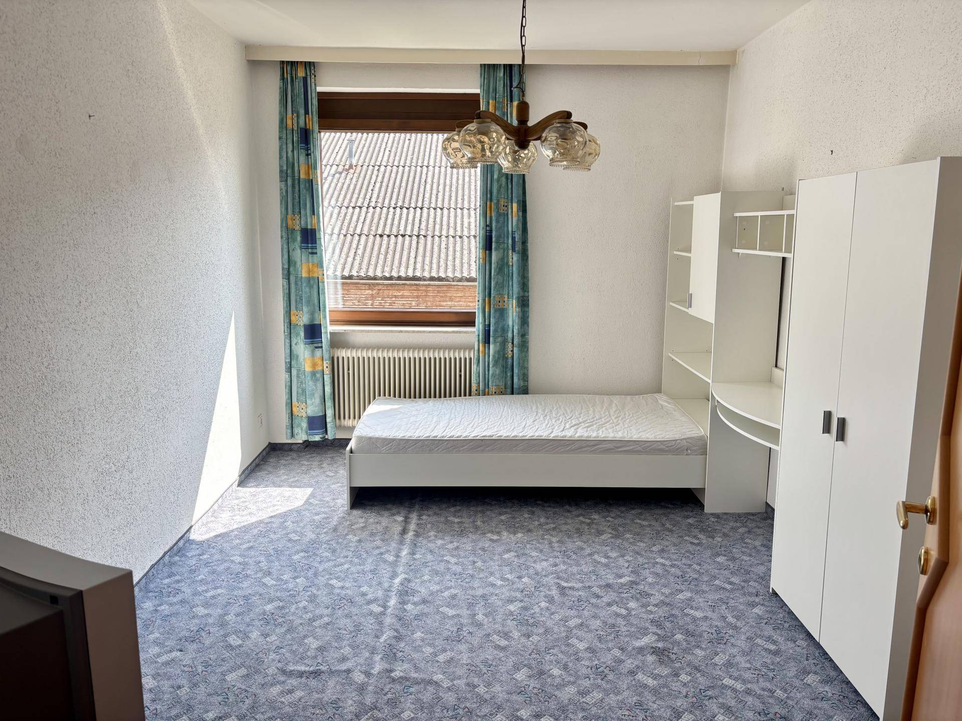 Schlafzimmer mit Teppichboden, Einzelbett und weißem Kleiderschrank, hell und funktional.