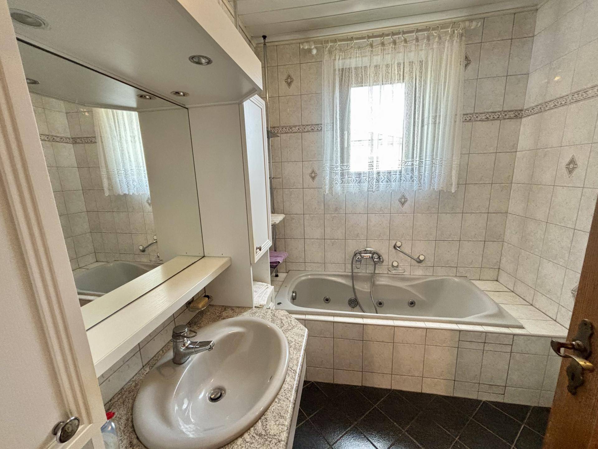 Badezimmer mit Whirlpool-Badewanne, Fliesen und Spiegelschrank, bietet Entspannung.