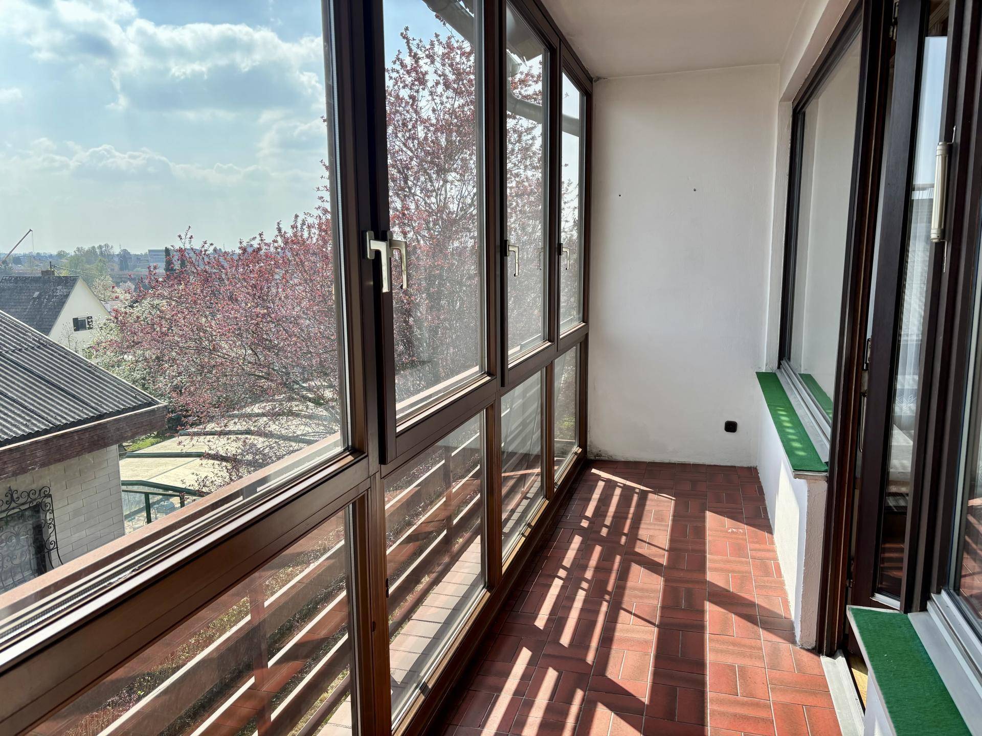 Verglaster Balkon, der als Wintergarten genutzt werden kann, mit Fliesenboden und Ausblick.