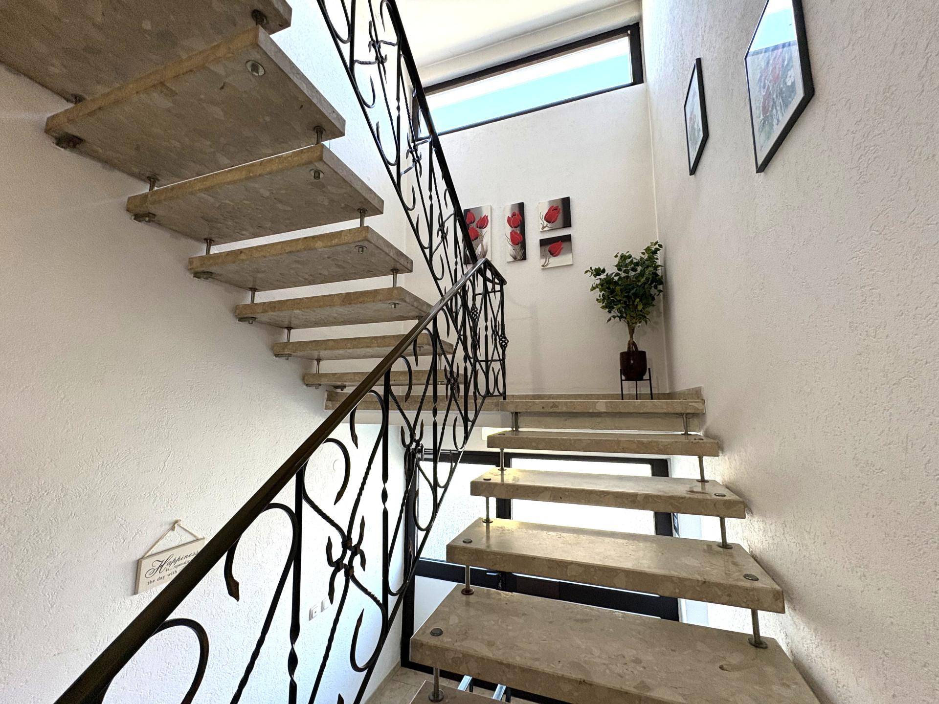 Elegante Steintreppe mit schmiedeeisernem Geländer und natürlichem Lichteinfall.