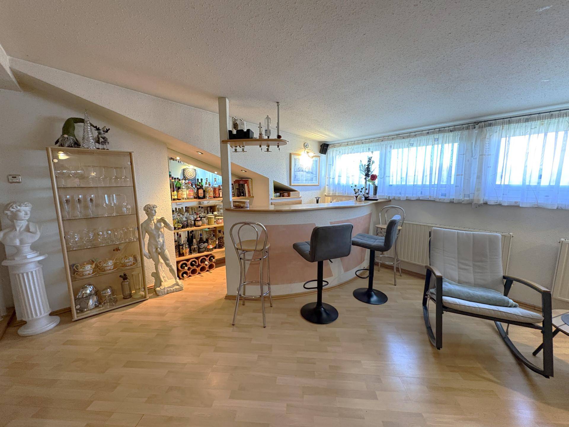 Heller Wohnbereich mit Bar, Holzboden und großen Fenstern im Dachgeschoss.