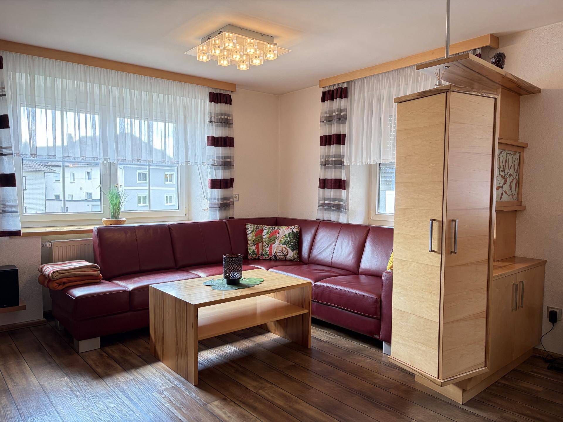 Wohnzimmer mit rotem Ledersofa, Holztisch und großen Fenstern für viel Tageslicht.