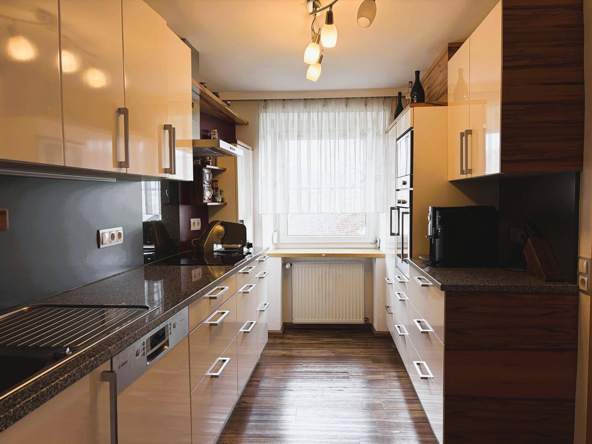 Moderne Küche mit glänzenden cremefarbenen Fronten, Granitarbeitsplatten und Fensterblick.