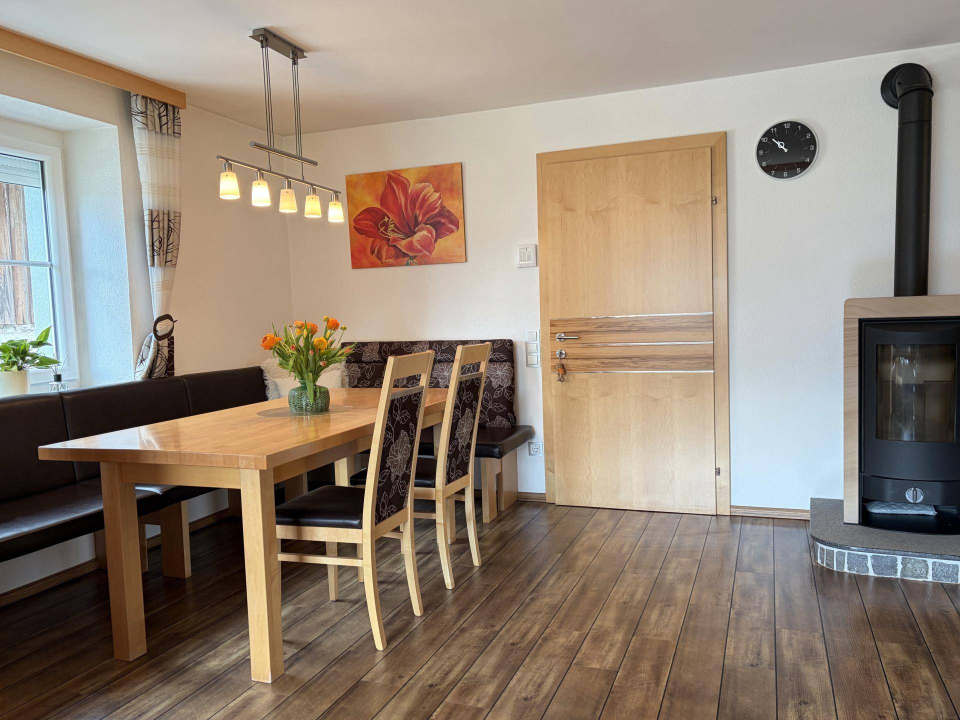 Gemütlicher Essbereich mit Holztisch, Eckbank und einem Kaminofen für warme Abende.